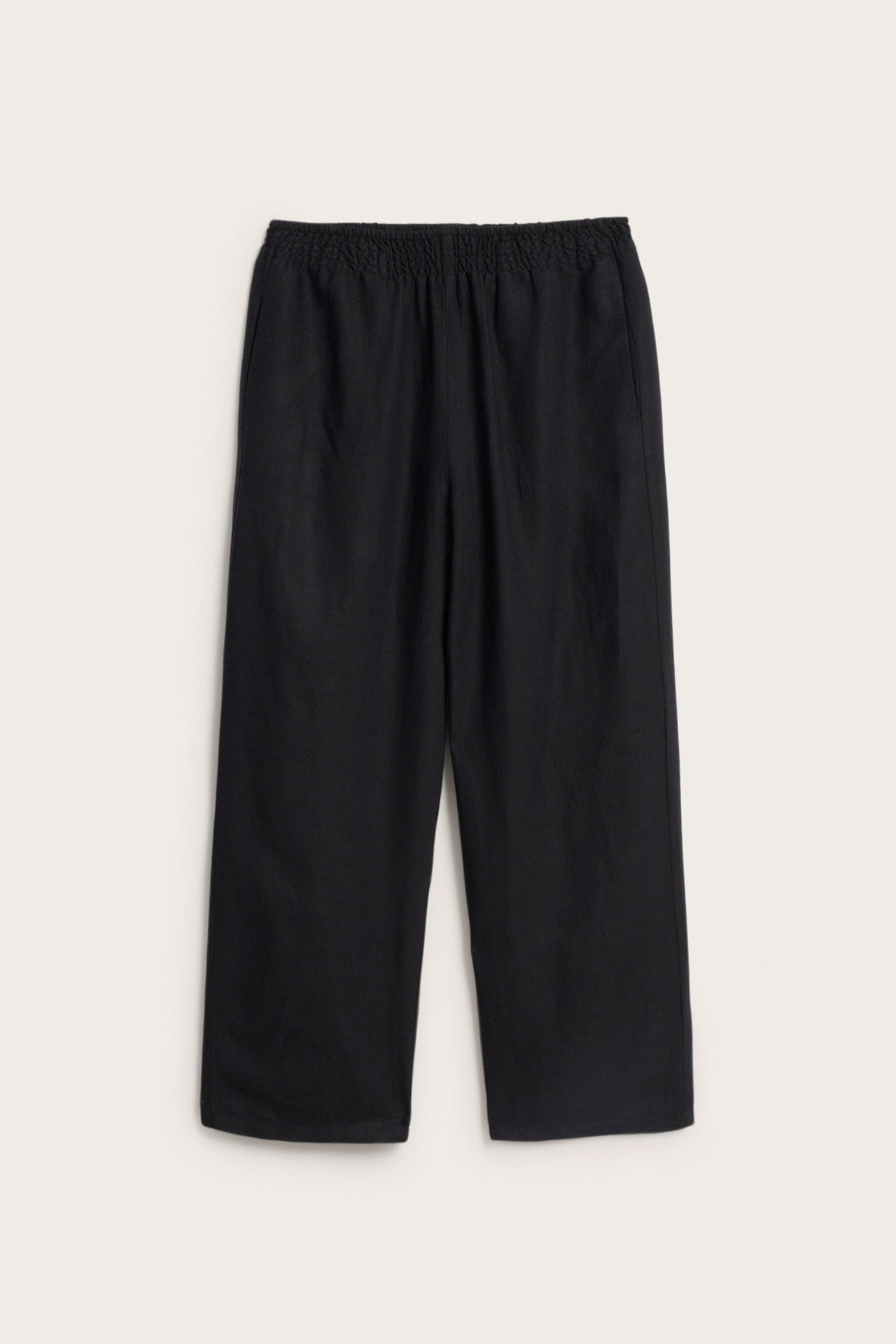 Frontbilde av sorte pull-on bukser i linblanding med smockstrikk i midjen og vide ben.