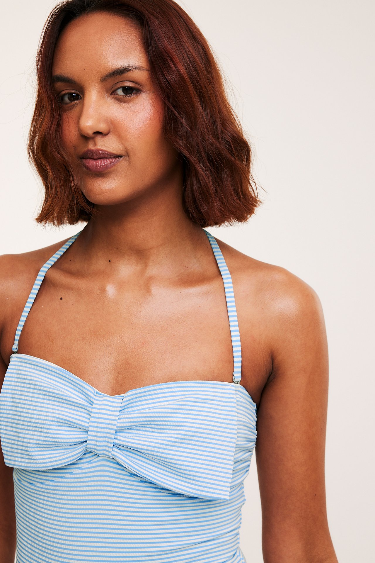 Zbliżenie, przód: kobieta w jasnoniebieskim kostiumie w paski z dużą kokardą i wiązaniem na szyi.