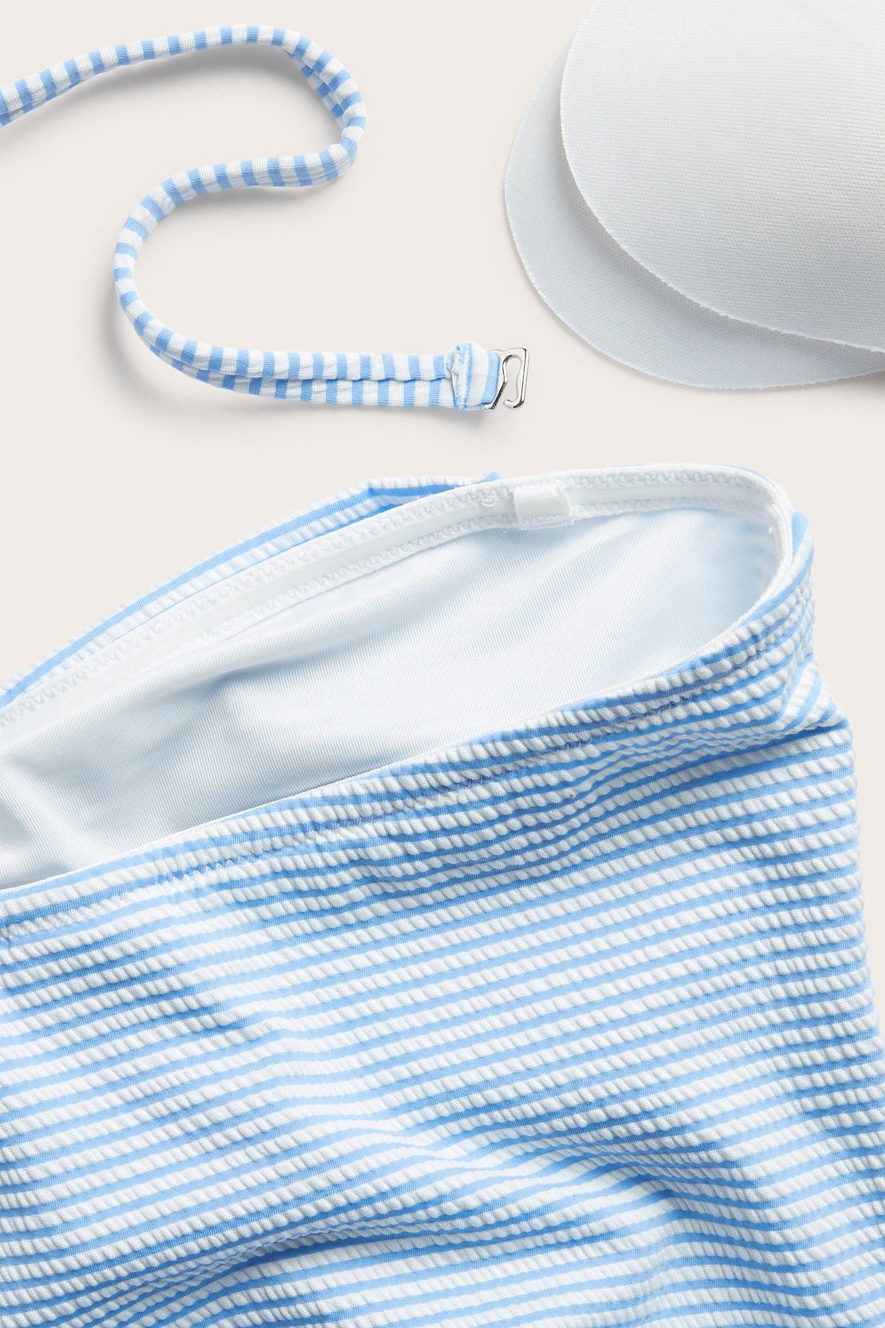 Närbild av blåvit randig baddräktsväv, en avtagbar axelrem och två vita bh-inlägg.
