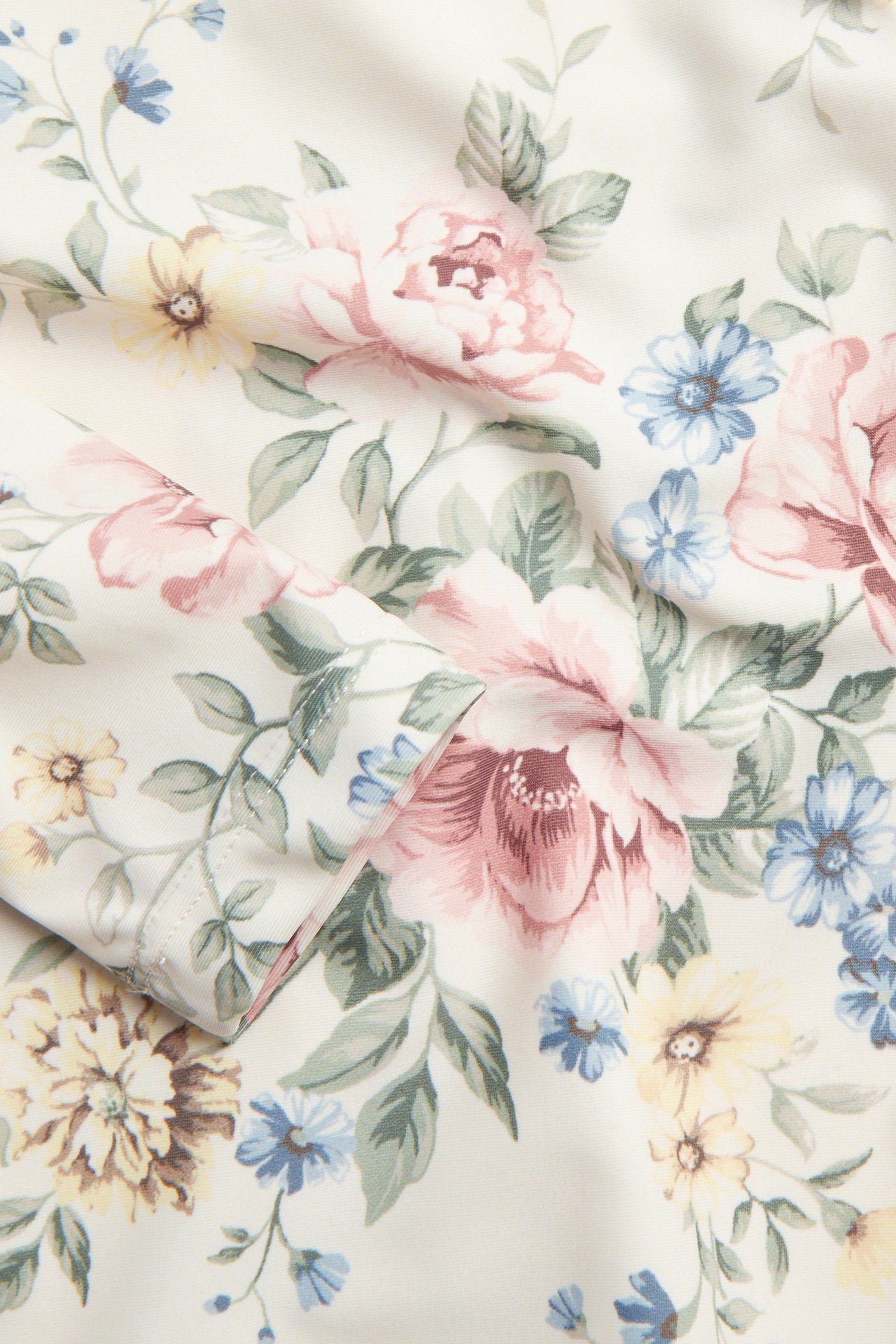 Närbild av offwhite UV-toppstyg med detaljerat rosa, blått och gult blommönster.