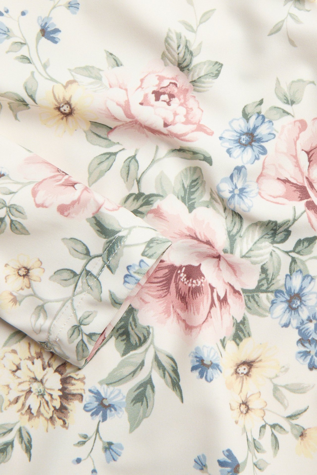 Nærbilde av offwhite UV-toppstoff med detaljert rosa, blått og gult blomstermønster.
