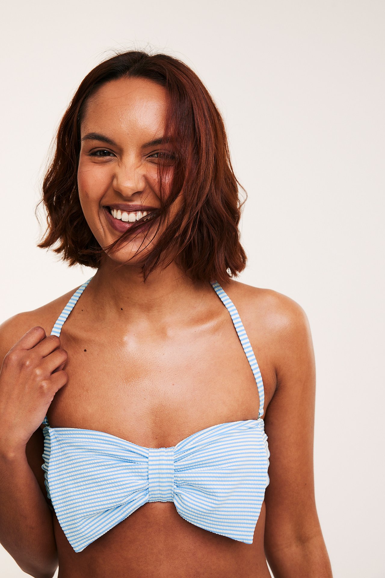 Edestäpäin: Nainen yllään raidallinen sinivalkoinen bikinin yläosa isolla rusetilla ja niskalenkeillä.