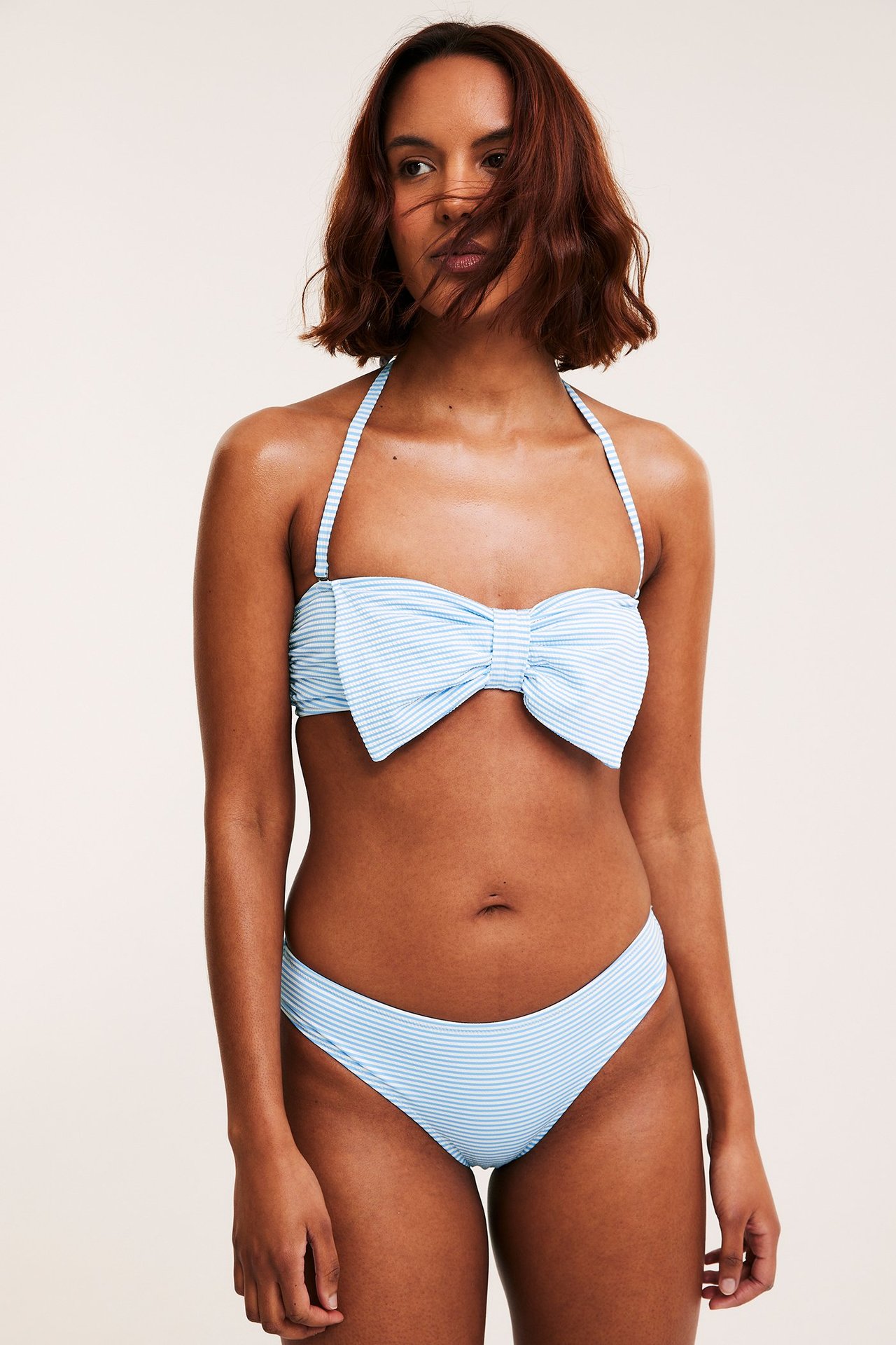 Widok z przodu kobiety w pasiastych niebiesko-białych majtkach bikini i dopasowanym topie bandeau z kokardą.