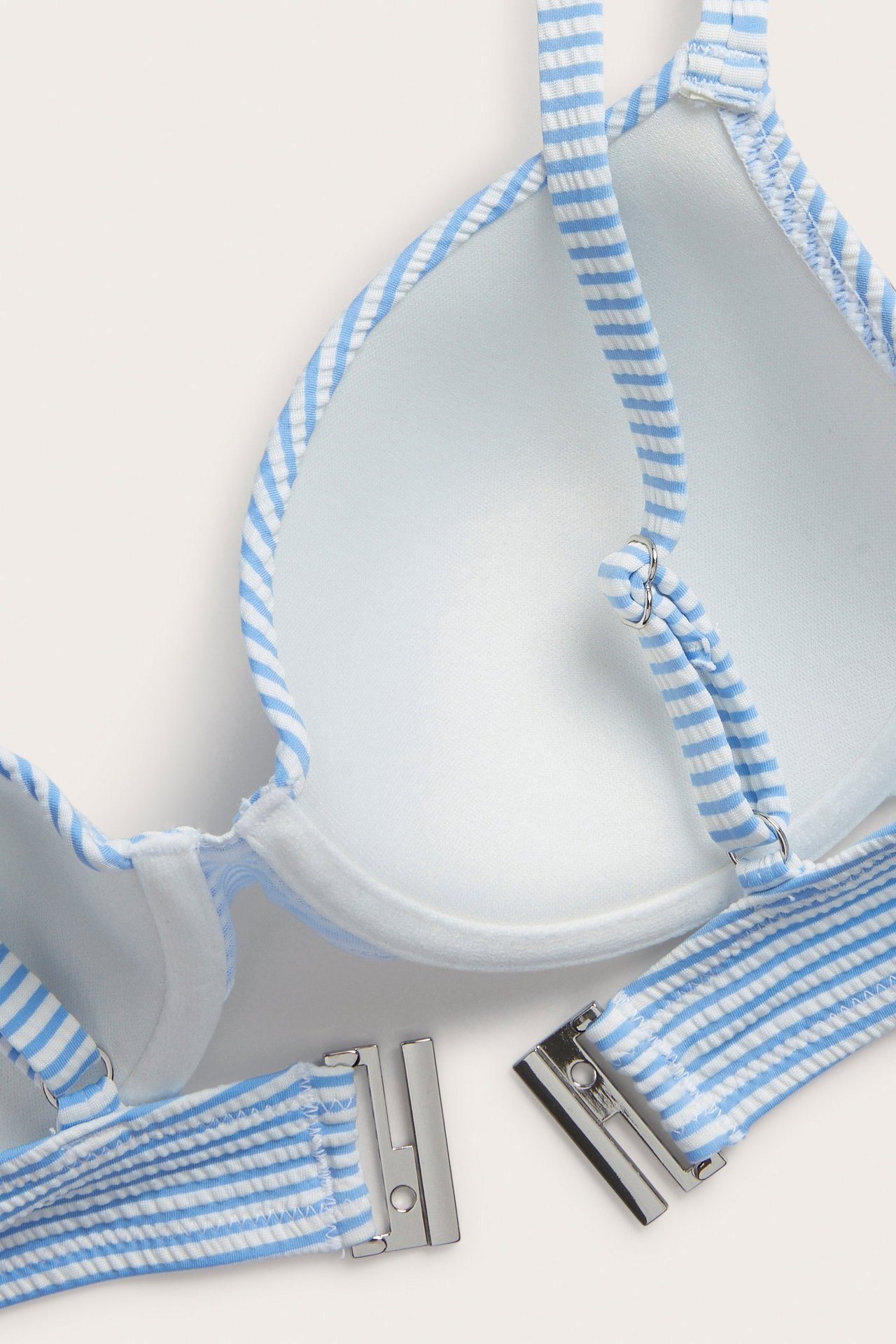 Lähikuva sinivalkoraidallisista bikiniliiveistä, joissa on topatut kupit, säädettävät olkaimet ja takakiinnitys.
