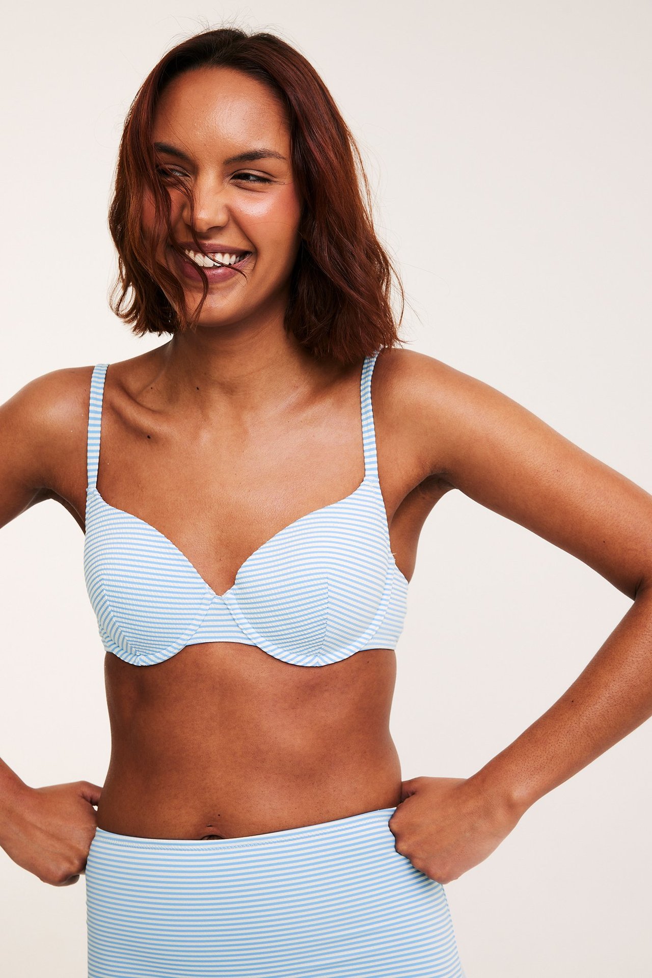Frontbilde av en kvinne i lys blått og hvitt stripet bikinitopp med formede cuper og matchende underdel.