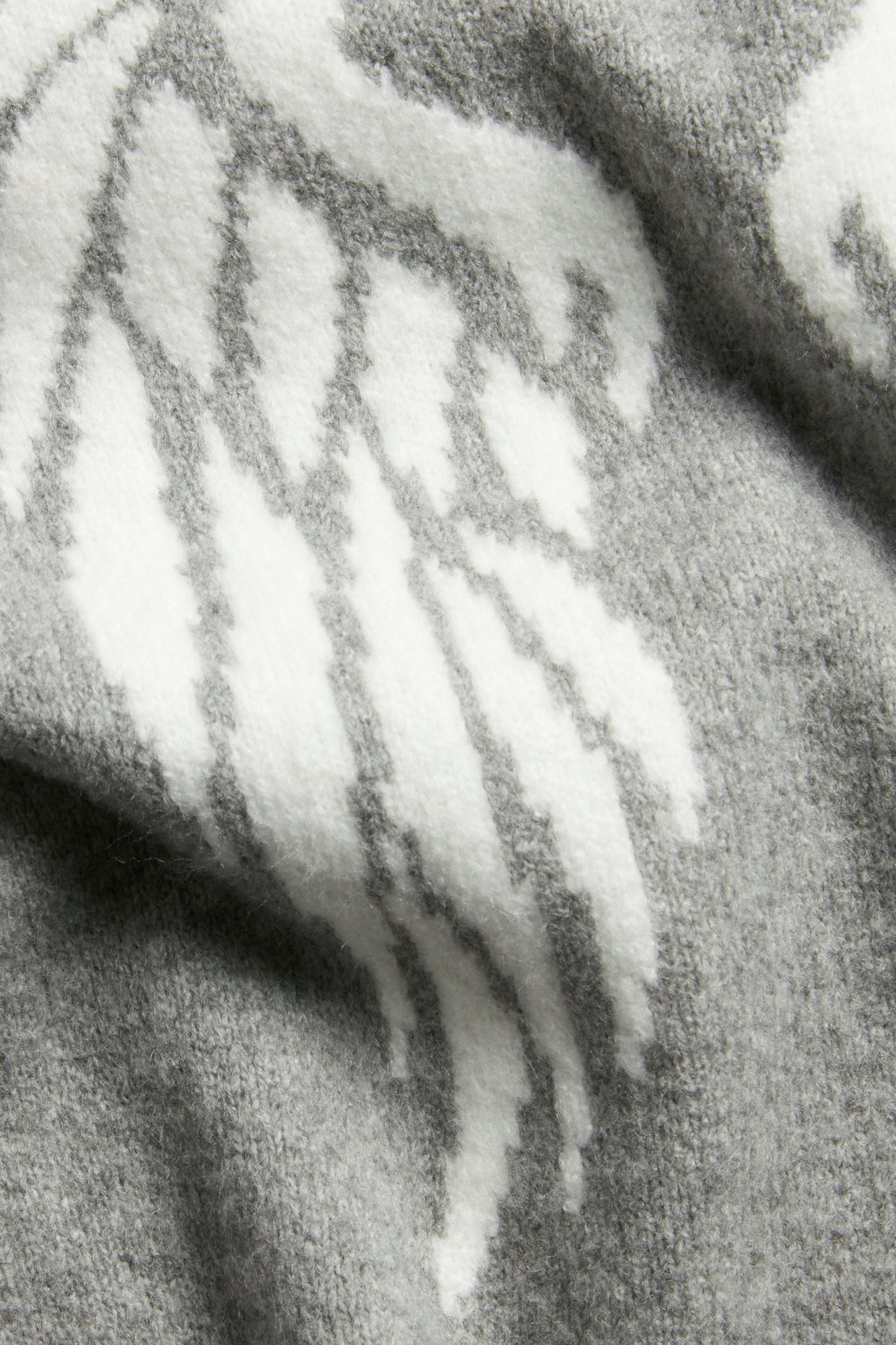 Nærbilde av en lys grå finstrikket t-skjorte med et hvitt jacquardmønster av vinger.