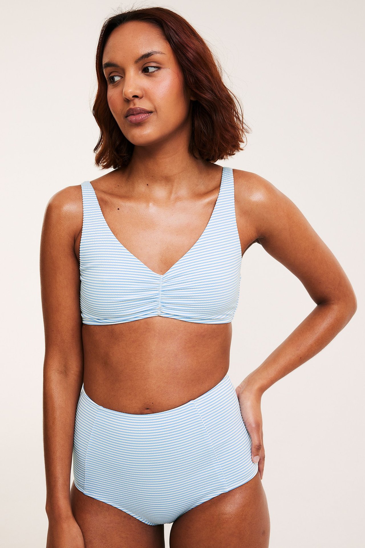 Frontbilde av en kvinne i en lys blå og hvitstripet bikini-BH med rynker og matchende bikinitruse.