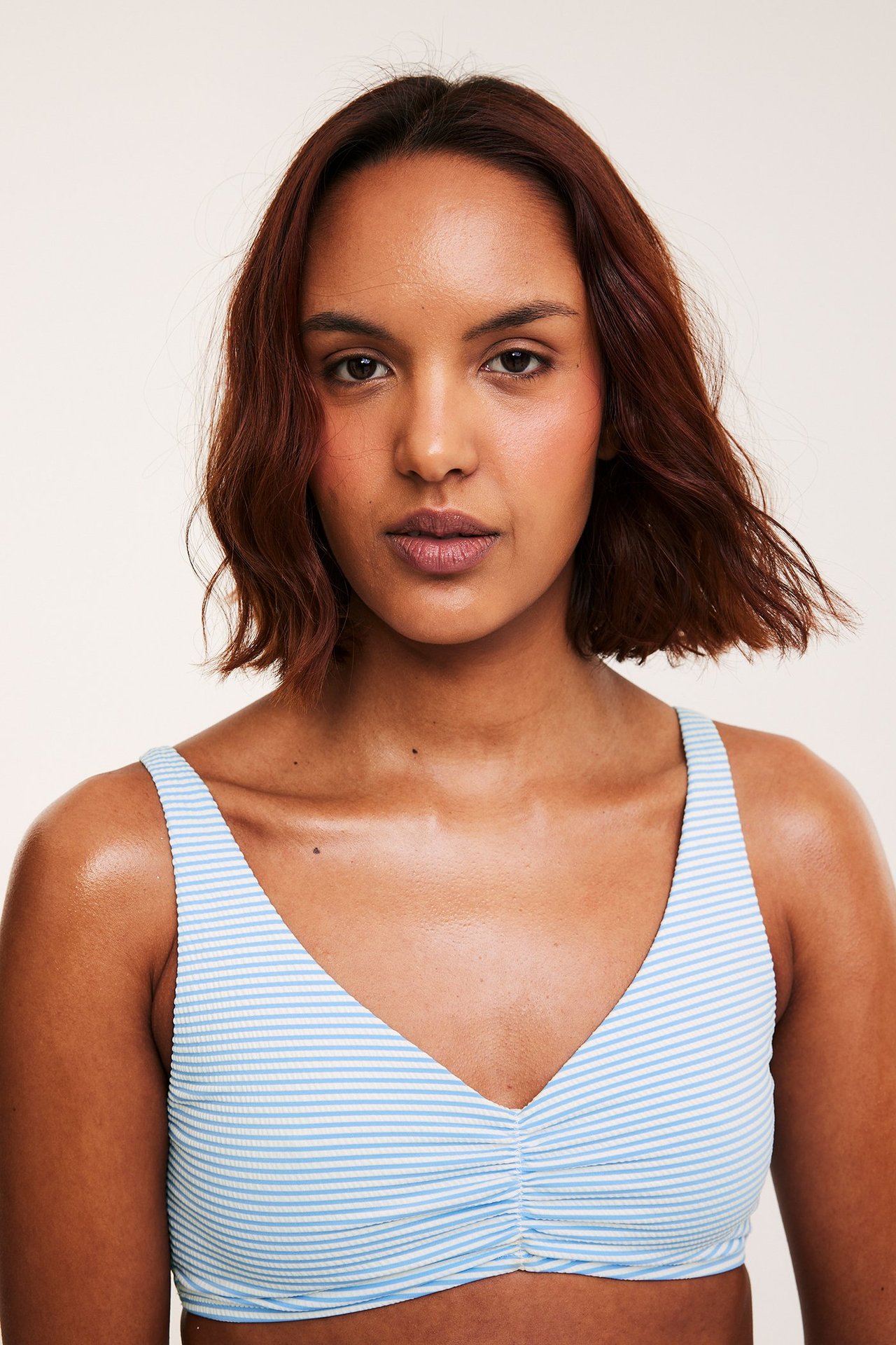 Frontbilde av en kvinne med stripet lys blå og hvit bikini-BH med rynket front og brede stropper.