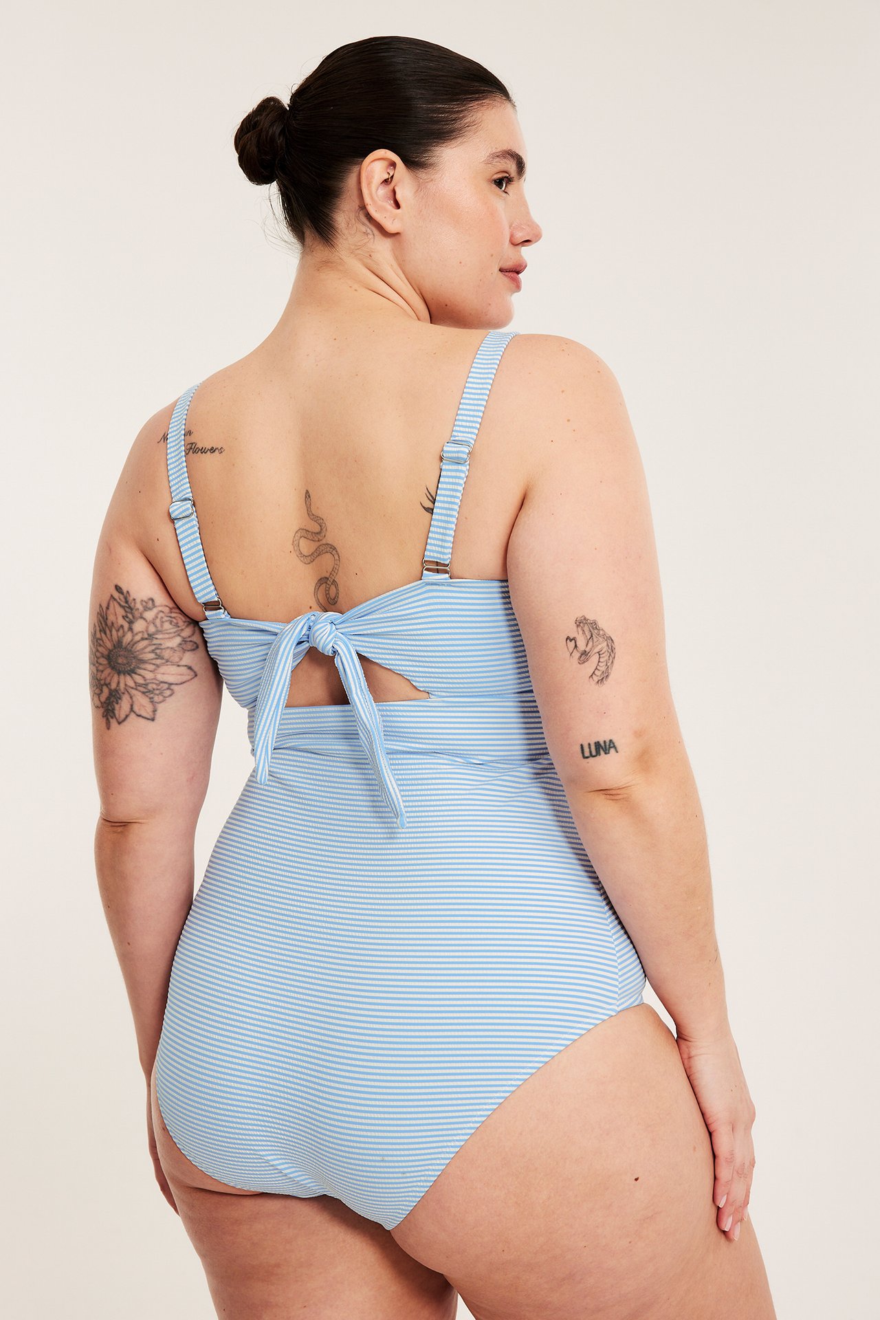 Bakifrån på en kvinna i en ljusblåvit randig baddräkt med justerbara axelband och knyt baktill.