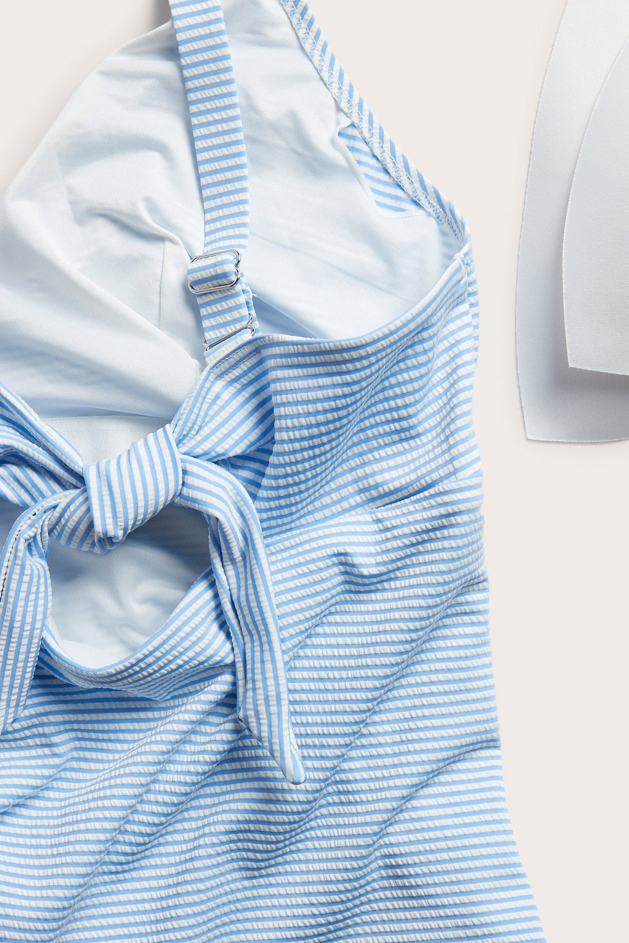 Närbild av ljusblå- och vitrandig baddräkt med texturerat tyg, justerbara axelband och knyt baktill.
