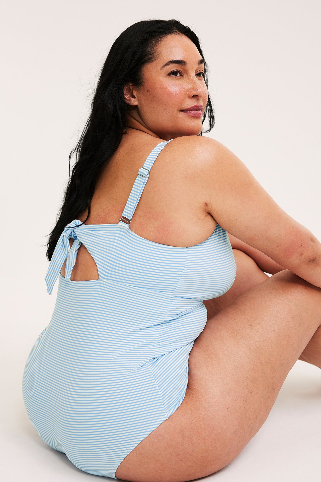 Bakfra: kvinne i lyseblå stripete badedrakt med justerbare stropper og knyting bak.