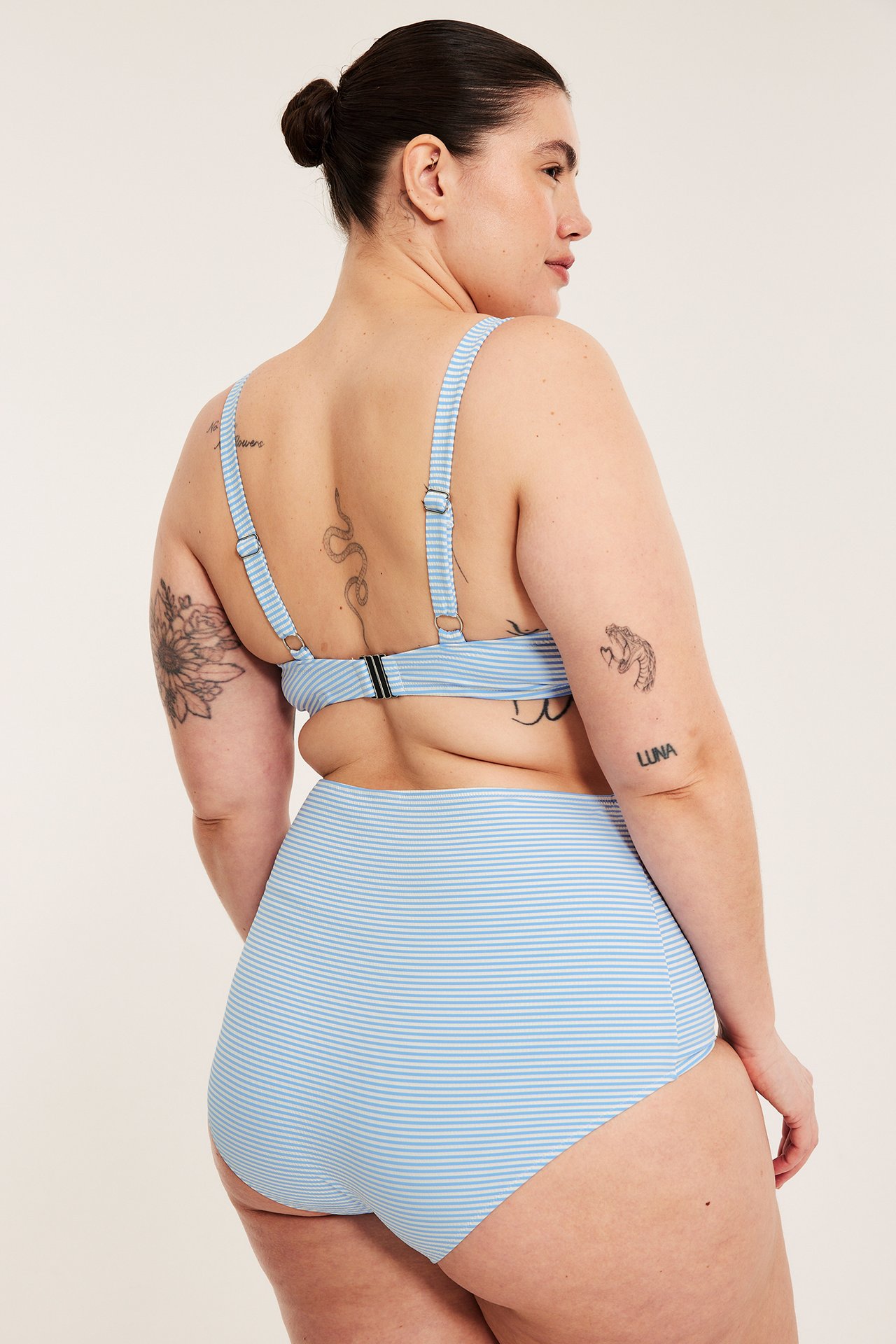 Bakfra: kvinne i lys blå og hvitstripet høy midje bikinitruse og matchende bikinitopp.