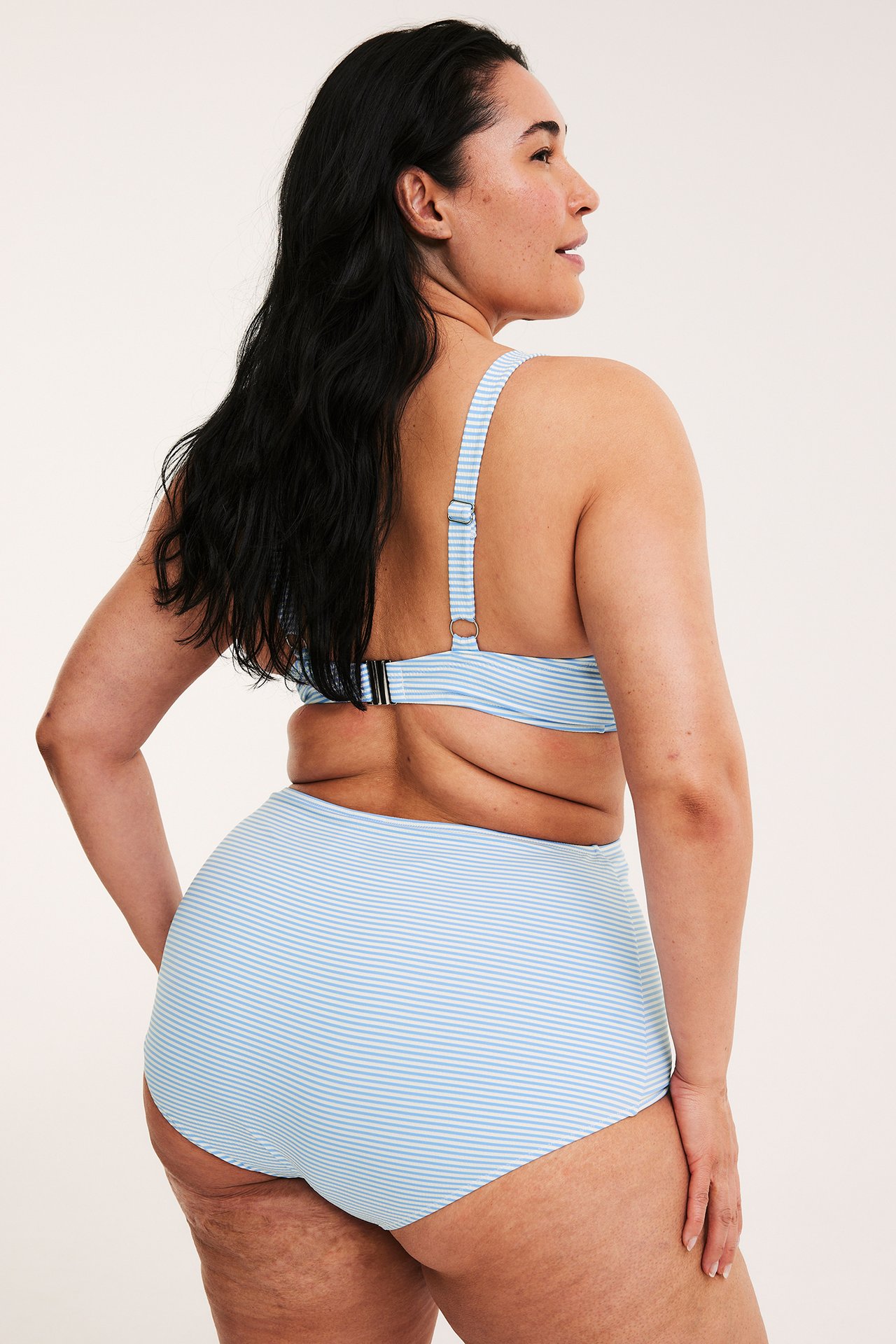 Takakuva naisesta, yllään vaaleansiniset-valkoiset raidalliset korkeavyötäröiset bikinialaosat ja yhteensopiva yläosa.