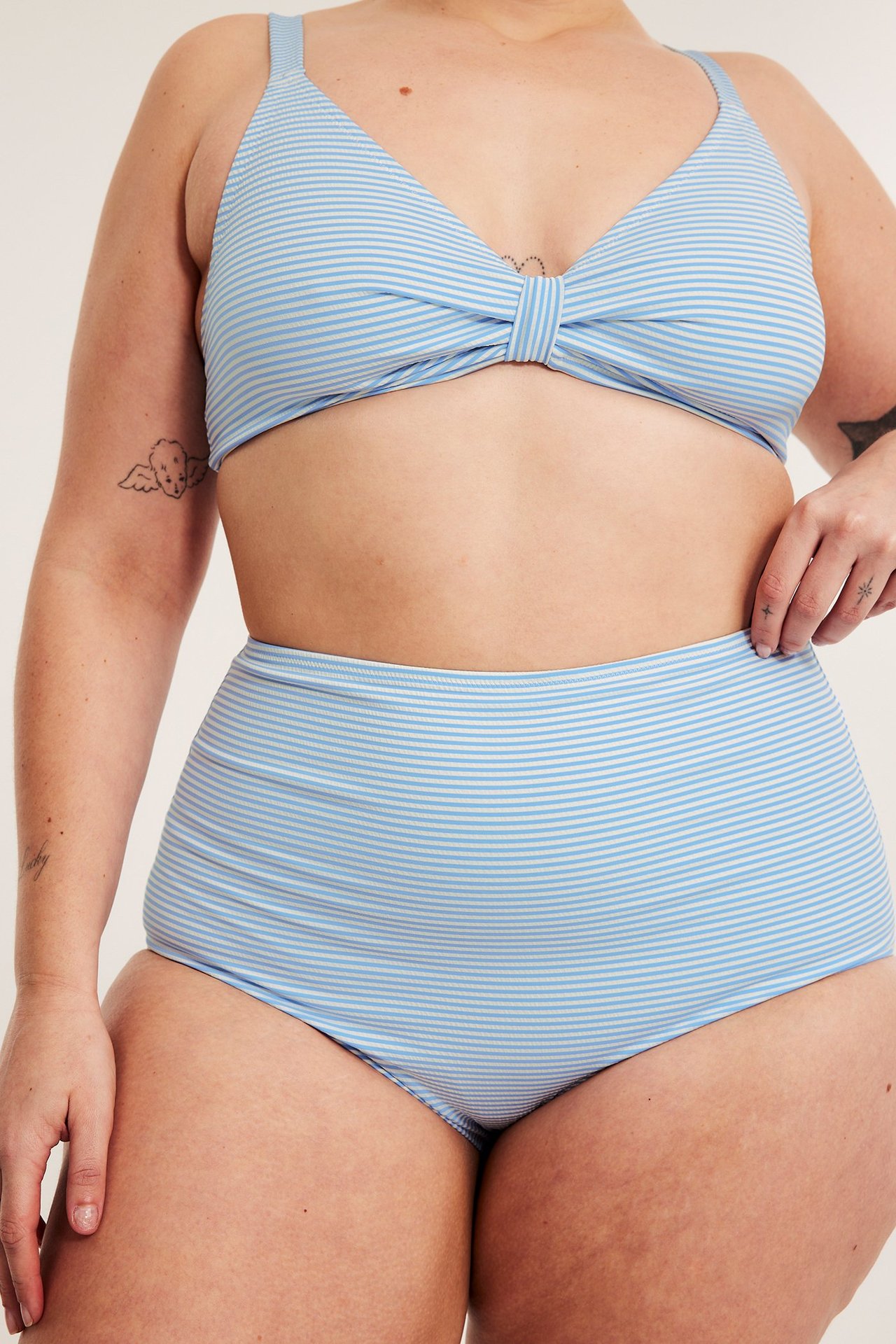 Naisen etukuva vaaleansinisessä raidallisessa korkeavyötäröisessä bikinialaosassa ja solmittavassa yläosassa.