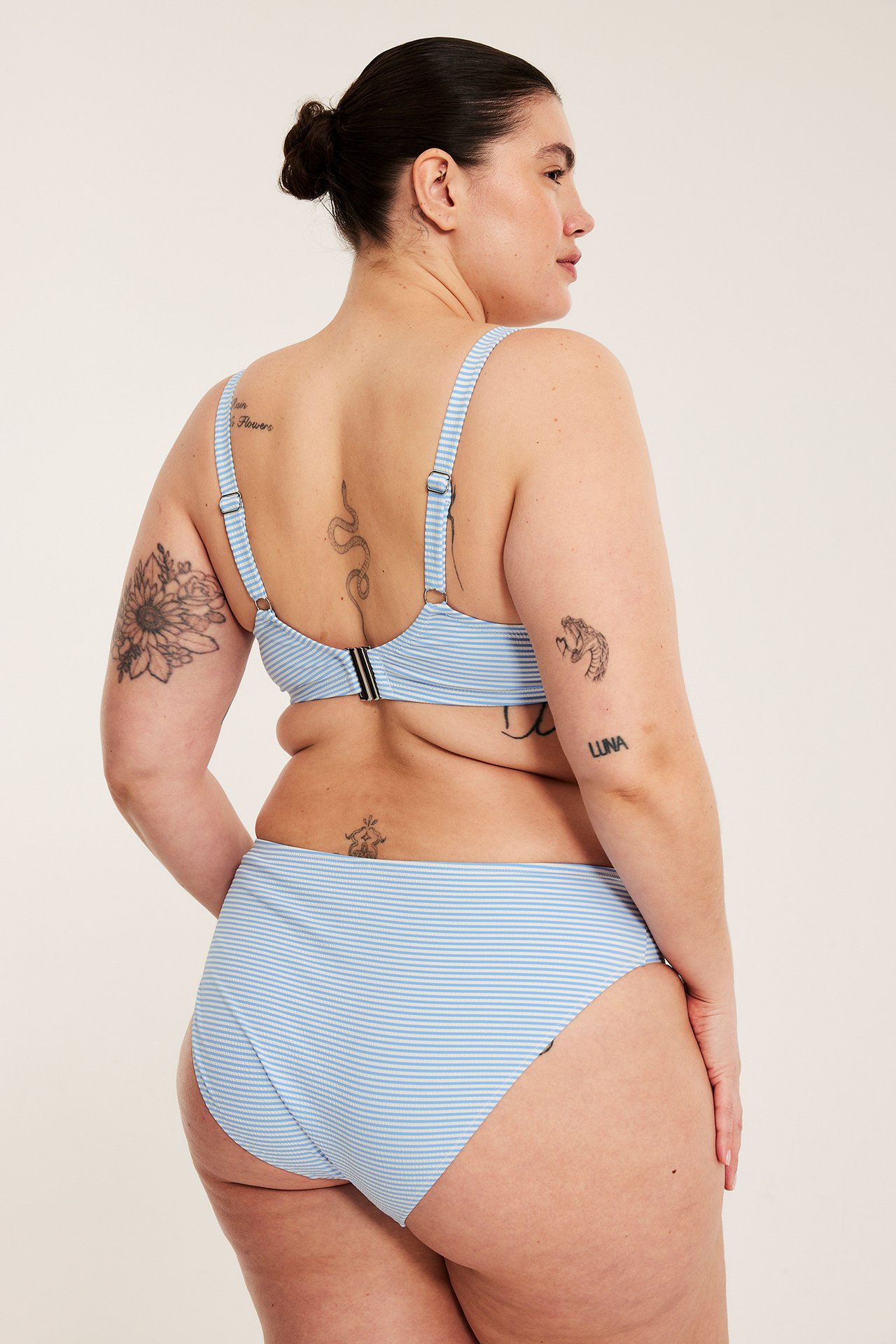Bakfra: Kvinne i lyseblå stripet bikinitruse og matchende bikinitopp med ryggspenne.