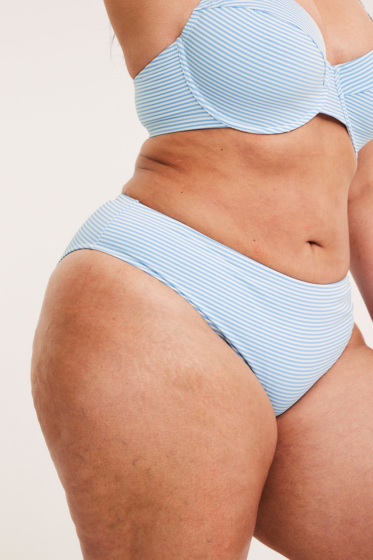 Sivukuva naisesta yllään vaaleansinivalkoraidalliset bikinialaosat ja yhteensopiva bikinitoppi.