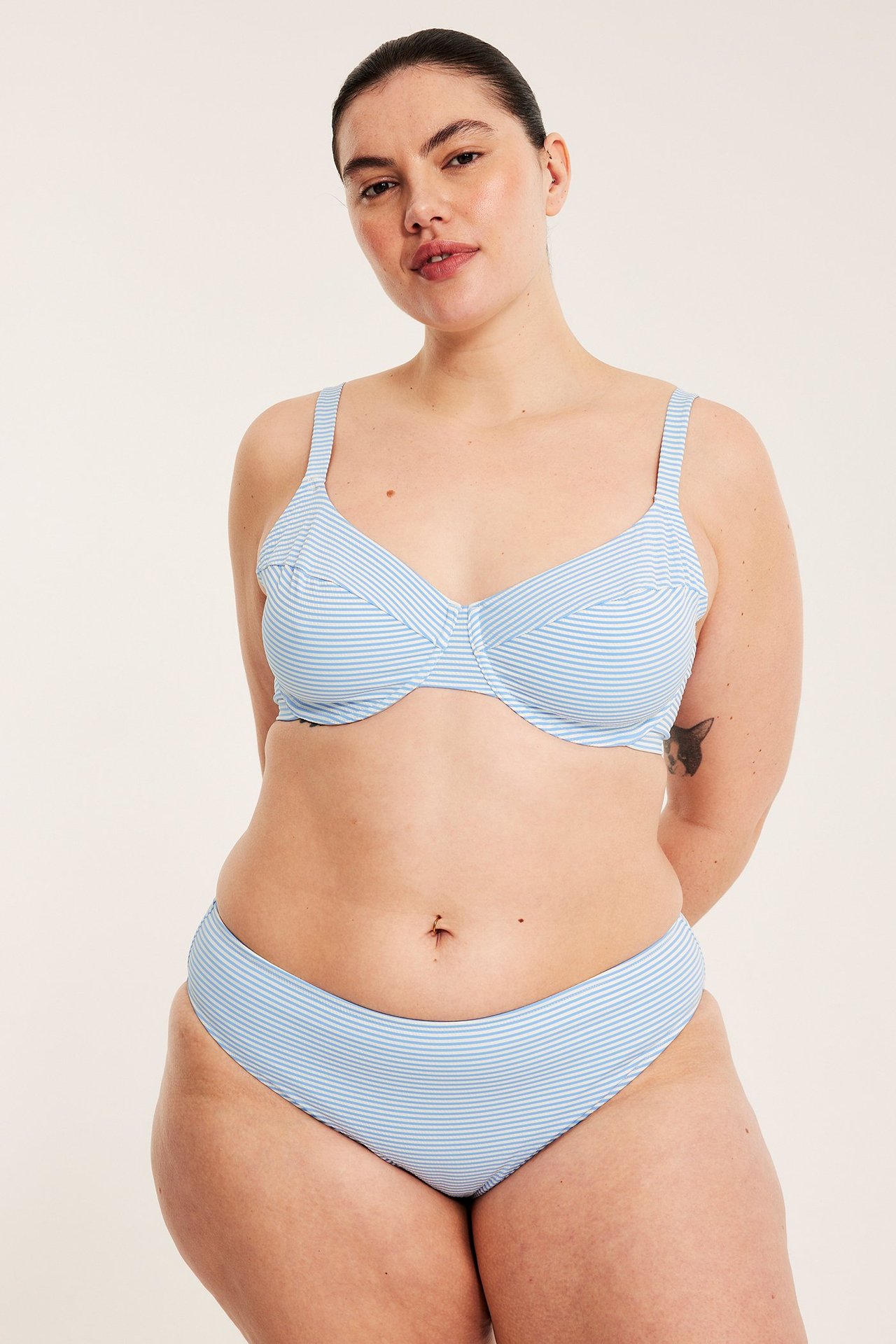 Edestäpäin nainen vaaleansinivalkoraidallisissa bikinialaosassa ja yhteensopivassa yläosassa.
