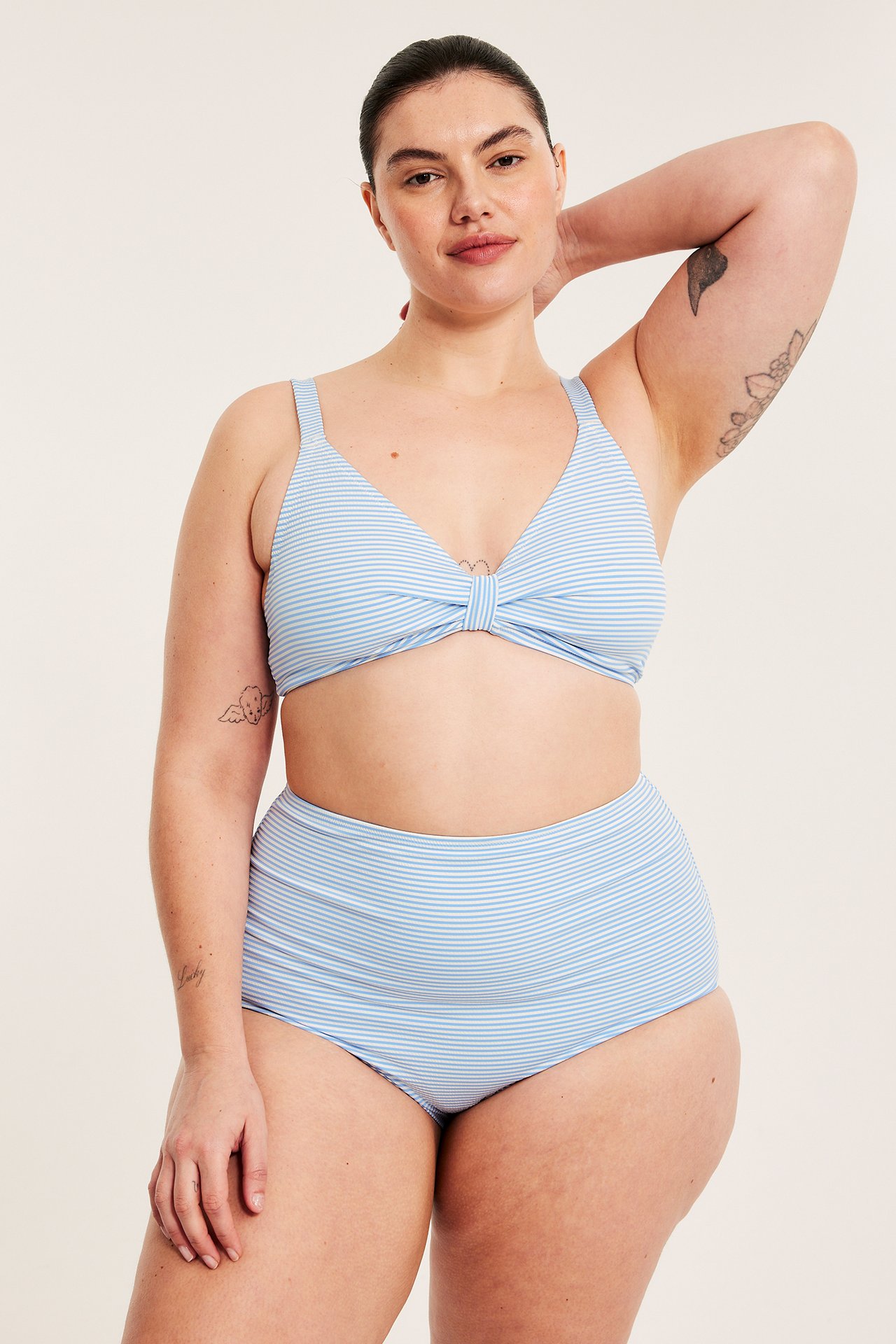 Edestä, nainen vaaleansinisessä raidallisessa bikiniyläosassa, solmulla edessä, ja korkeavyötäröisissä alaosissa.