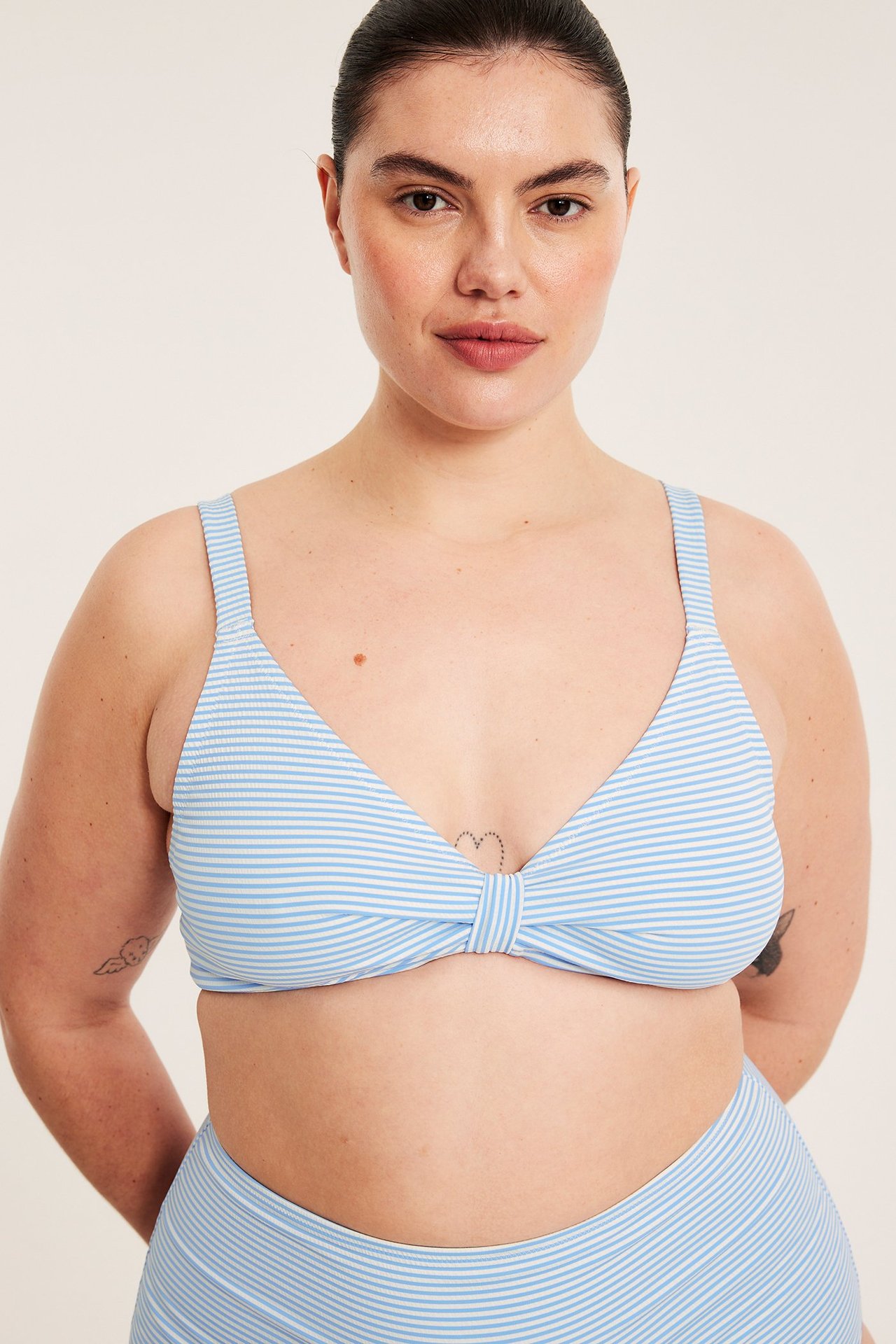 Edestä kuvattuna: Nainen yllään vaaleansininen raidallinen bikinitoppi solmulla, säädettävillä olkaimilla, ja yhteensopivat alaosat.