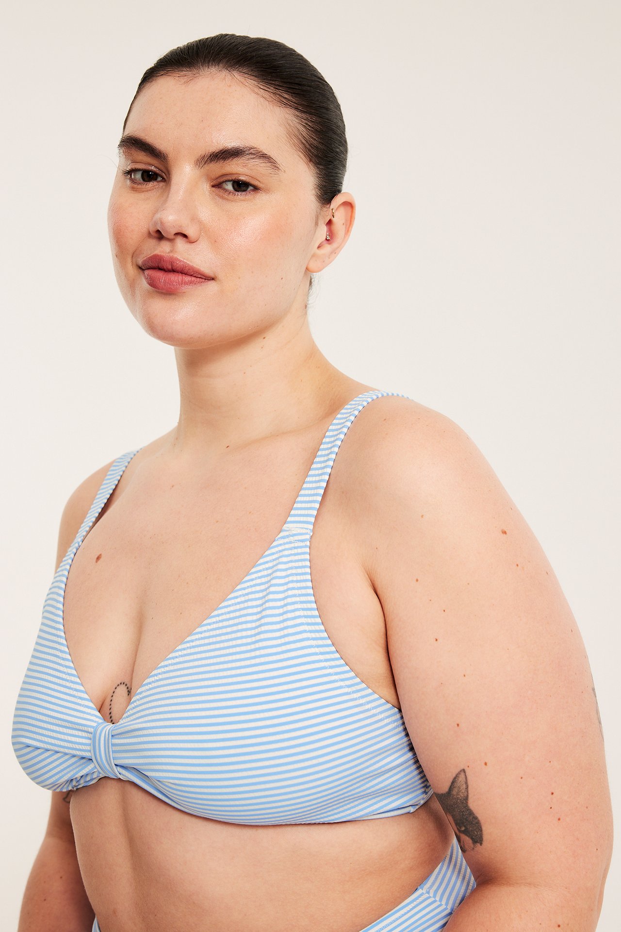 Lähikuva edestä naisesta, jolla on vaaleansinivalkoinen raidallinen bikiniyläosa solmuyksityiskohdalla edessä.