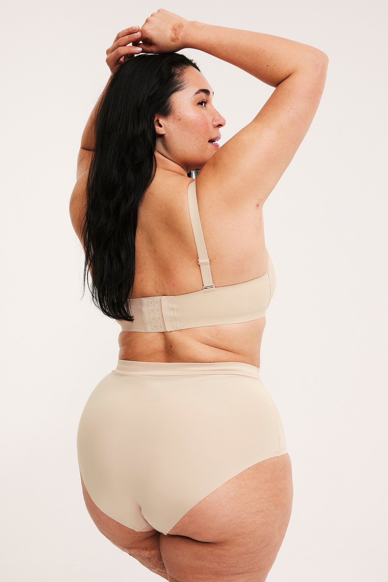 Bakifrån av kvinna i ljusbeige sömlösa hipstertrosor med resår i midjan och matchande BH.