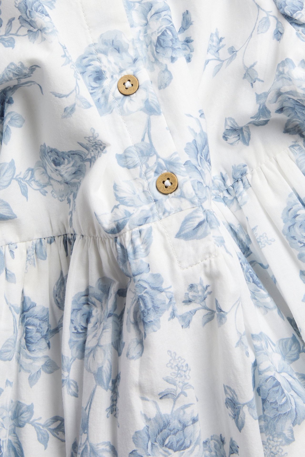 Zbliżenie ecru tkanej sukienki z niebieskim wzorem kwiatowym i jasnobrązowymi drewnianymi guzikami.