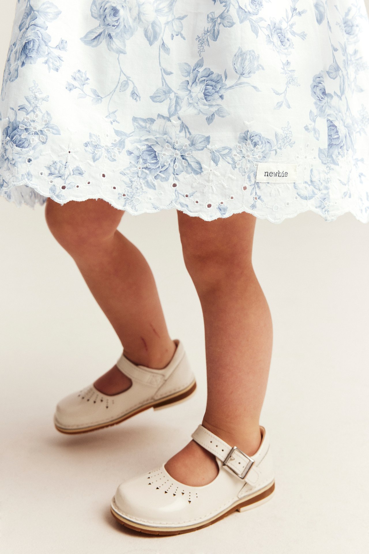 Nedre front: barn i offwhite blomsterkjole med broderi i kanten og offwhite Mary Jane-sko.