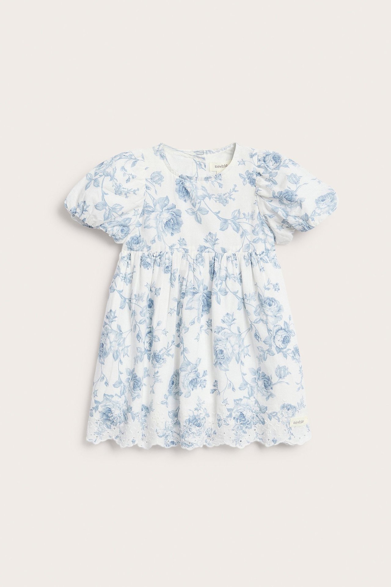 Forfra, barnekjole i offwhite med blått blomstermønster, puffermer og brodert bølgekant nederst.