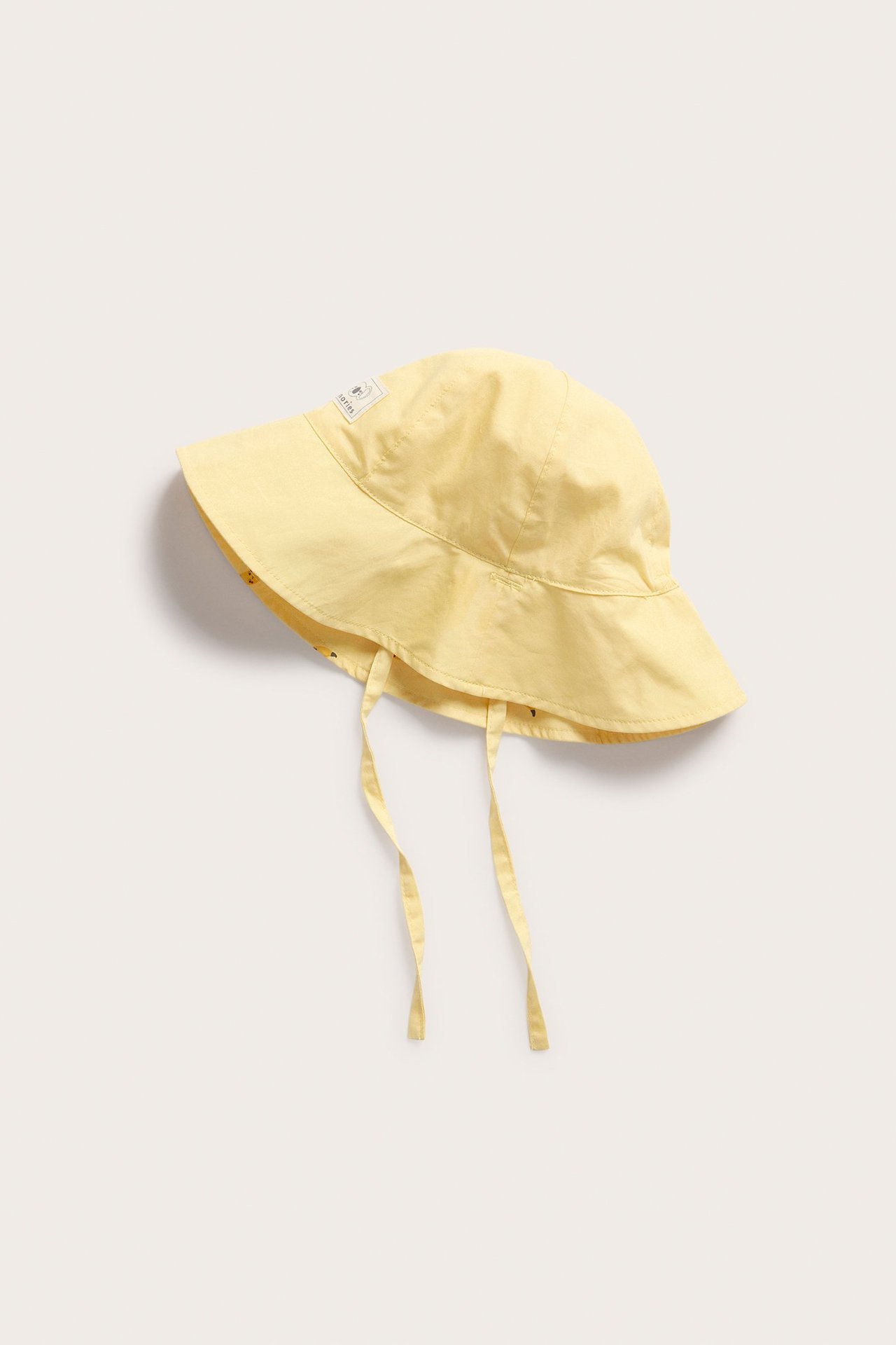 Viisto näkymä keltaisesta, käännettävästä vauvan aurinkohatusta puuvillaisilla solmimisnauhoilla.