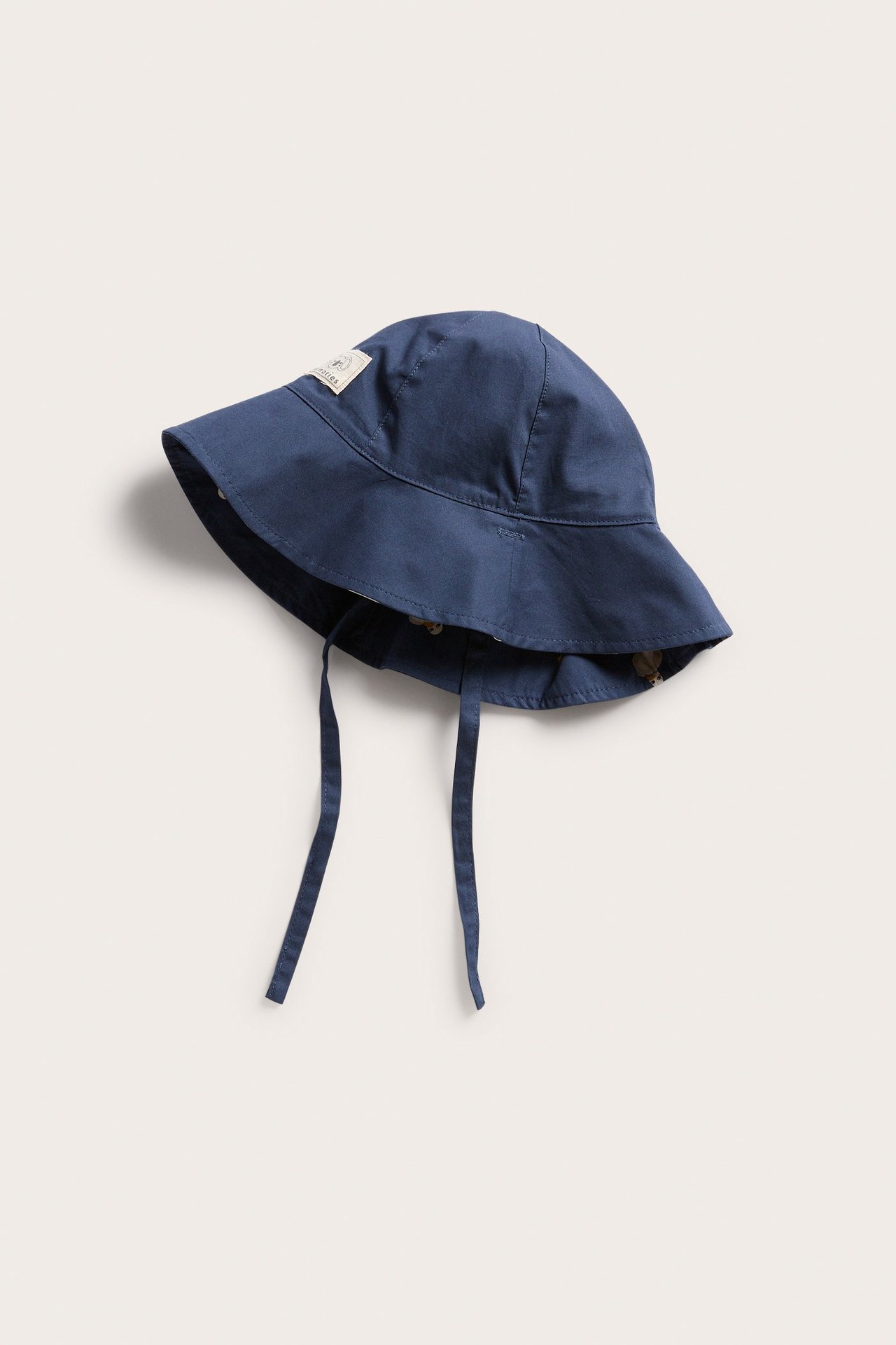 Edestä käännettävä tummansininen puuvillainen vauvan aurinkohattu ankkakuviovuorilla ja nauhoilla.
