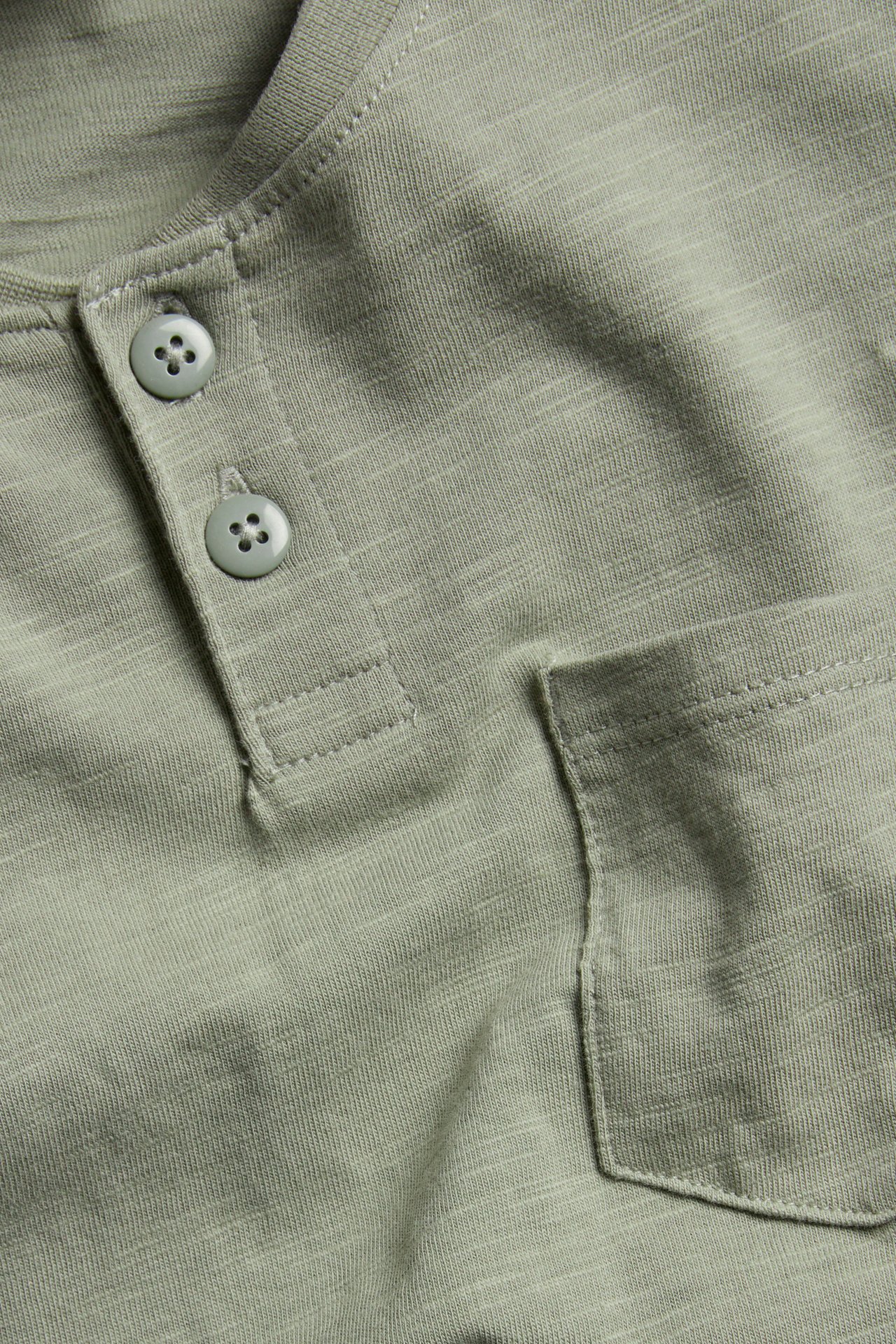 Zbliżenie zielonej koszulki Henley ze slubu, z prążkowaną listwą guzikową i kieszenią na piersi.