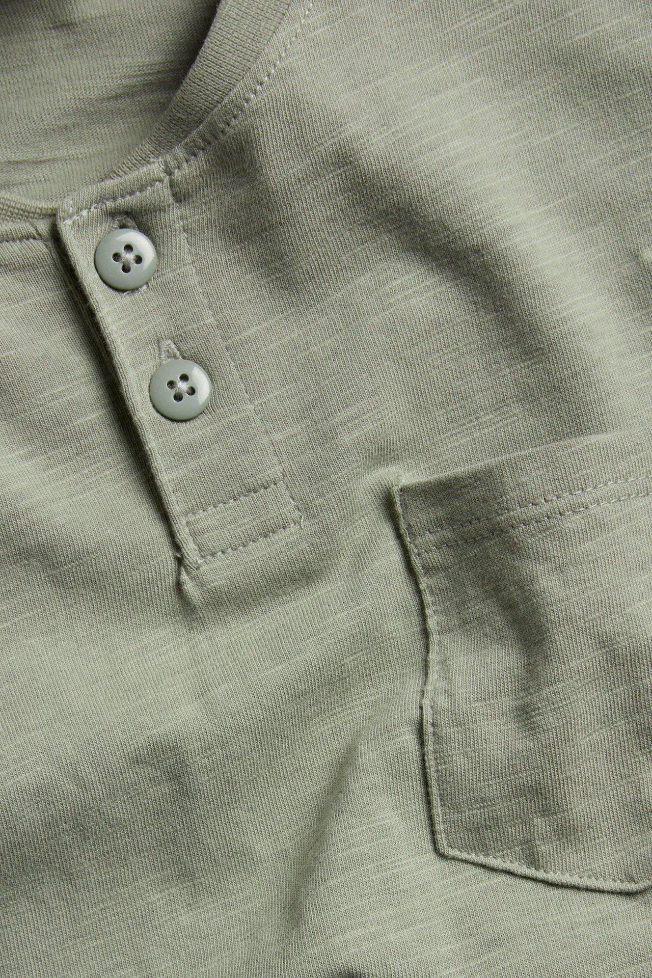 Zbliżenie zielonej koszulki Henley ze slubu, z prążkowaną listwą guzikową i kieszenią na piersi.