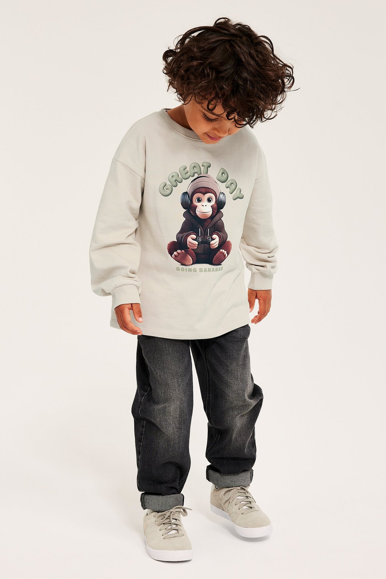 Edestä: Lapsi yllään beige collegepaita apinaprintillä, tummanharmaat farkut ja vaaleanbeiget tennarit.