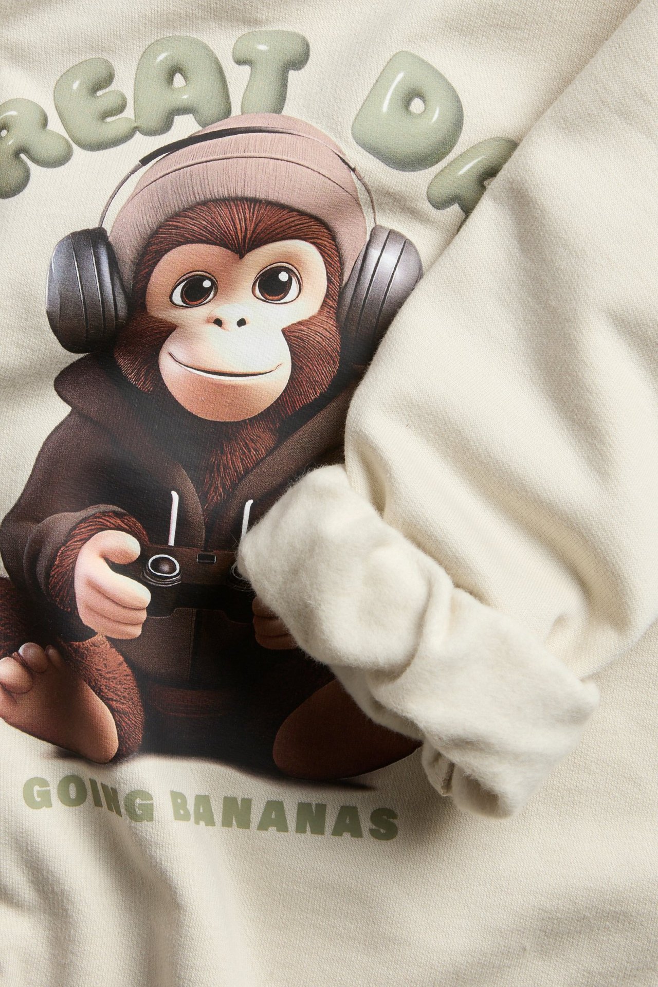 Beige collegepaita painokuvalla, ribbat kaula- ja hihansuut, lapsi pitää kameraa.