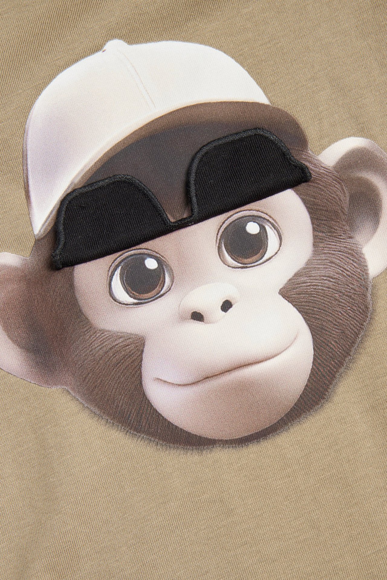 Närbild av en beige långärmad t-shirt med ett apskalleprint och lyftbara svarta solglasögon.