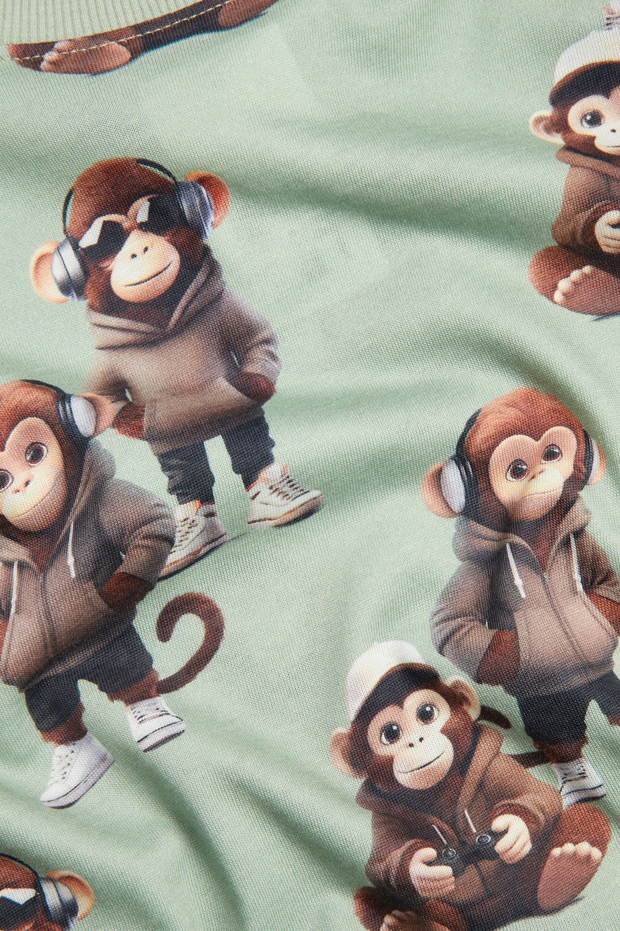 Zbliżenie: jasnozielona bawełniana koszulka z długim rękawem, z nadrukiem małp w bluzach.