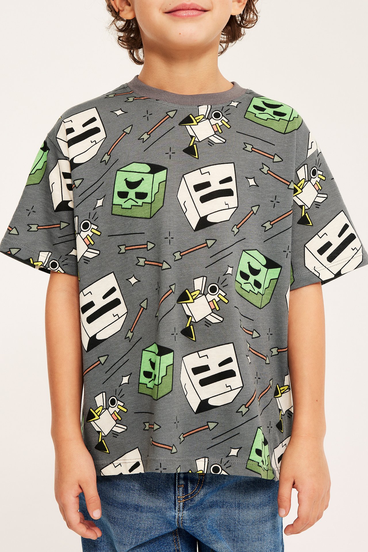 Edestäpäin kuvattu lapsi yllään harmaa Minecraft-kuvioinen puuvillainen T-paita ja siniset farkut.