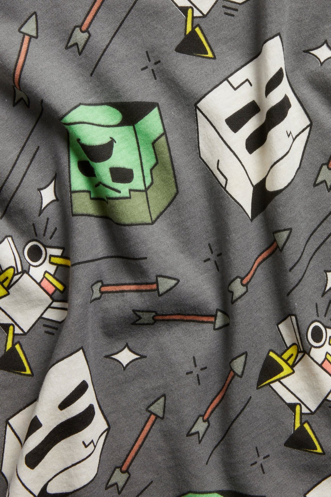 Zbliżenie na szary bawełniany T-shirt z nadrukiem Minecraft na całej powierzchni, przedstawiającym Creepery, szkielety i strzały.