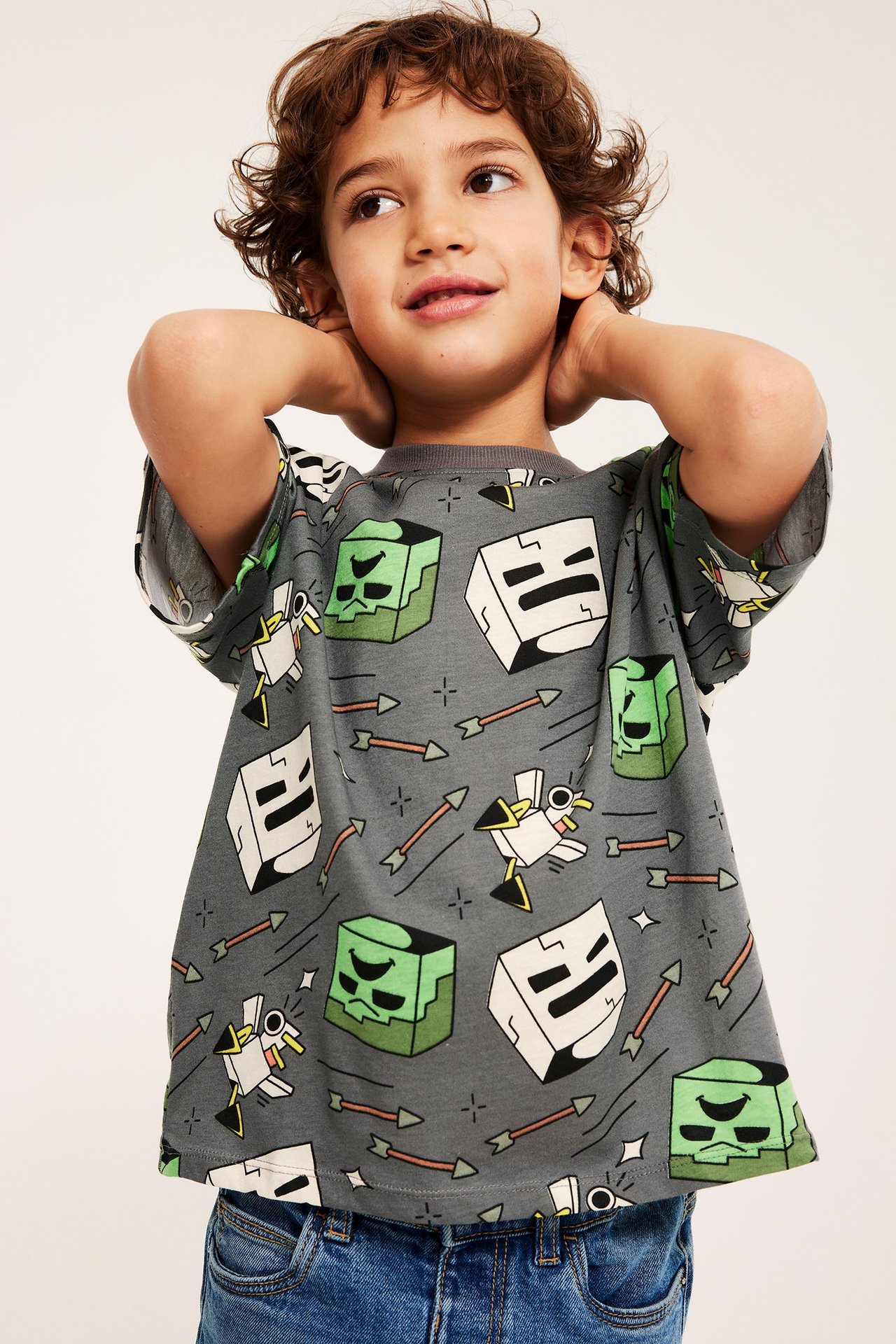 Edestäpäin: lapsi yllään harmaa puuvillainen Minecraft-kuvioinen T-paita ja siniset farkut.