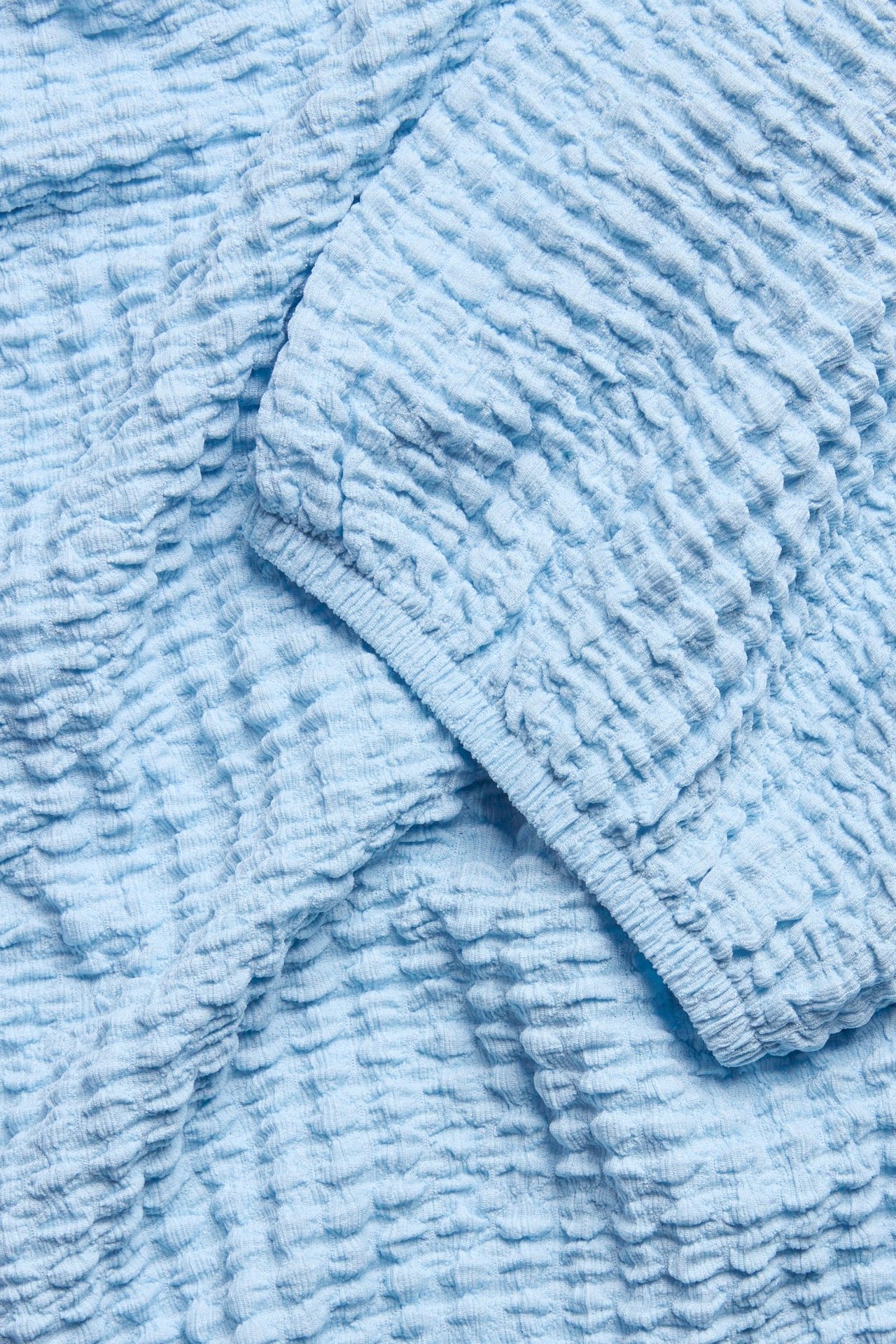 Zbliżenie jasnoniebieskiego topu z bufiastym rękawem z elastycznym mankietem.