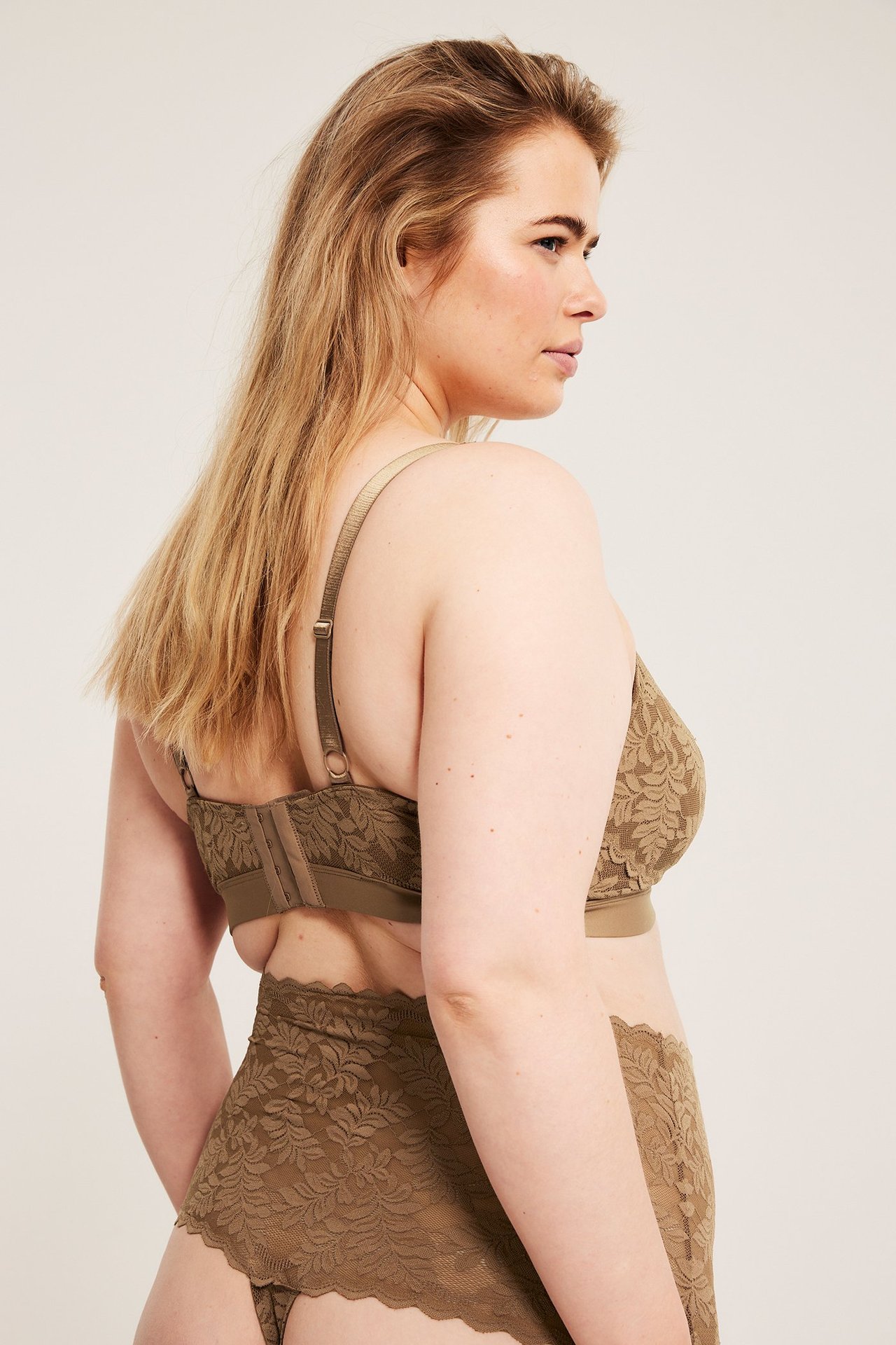 Widok z boku kobiety w brązowych koronkowych stringach z wysokim stanem i pasującym koronkowym biustonoszu.