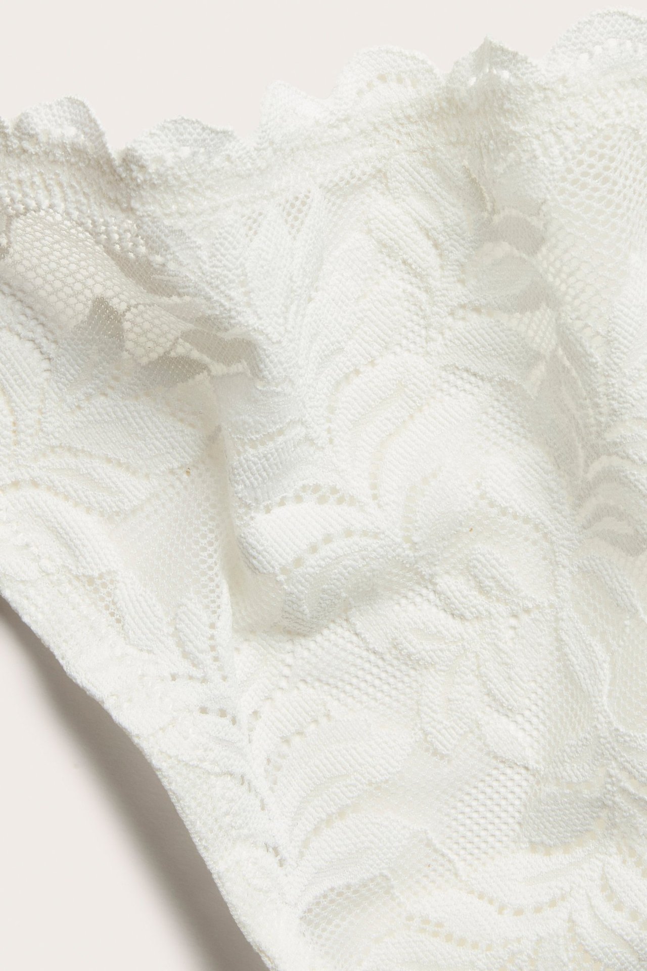 Zbliżenie beżowych koronkowych stringów z delikatnym kwiatowym wzorem.