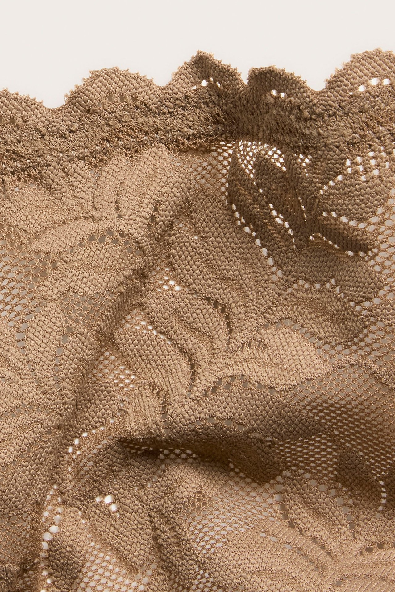 Zbliżenie brązowych koronkowych stringów z ozdobnym brzegiem, ukazujące miękki, rozciągliwy materiał.