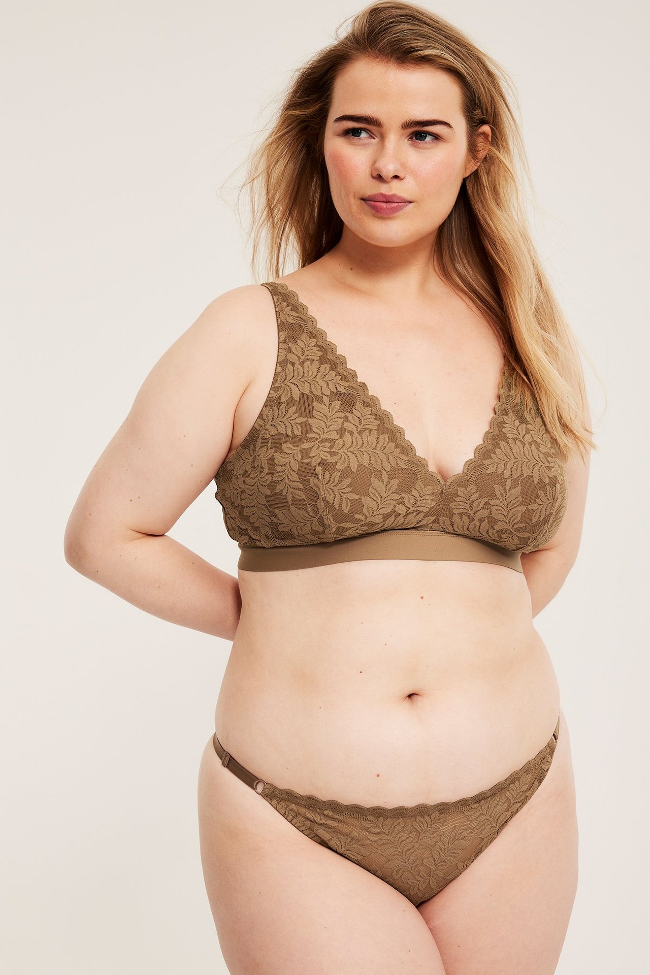 Przód: kobieta w brązowych koronkowych stringach z regulowanymi paskami bocznymi i pasującym biustonoszu.