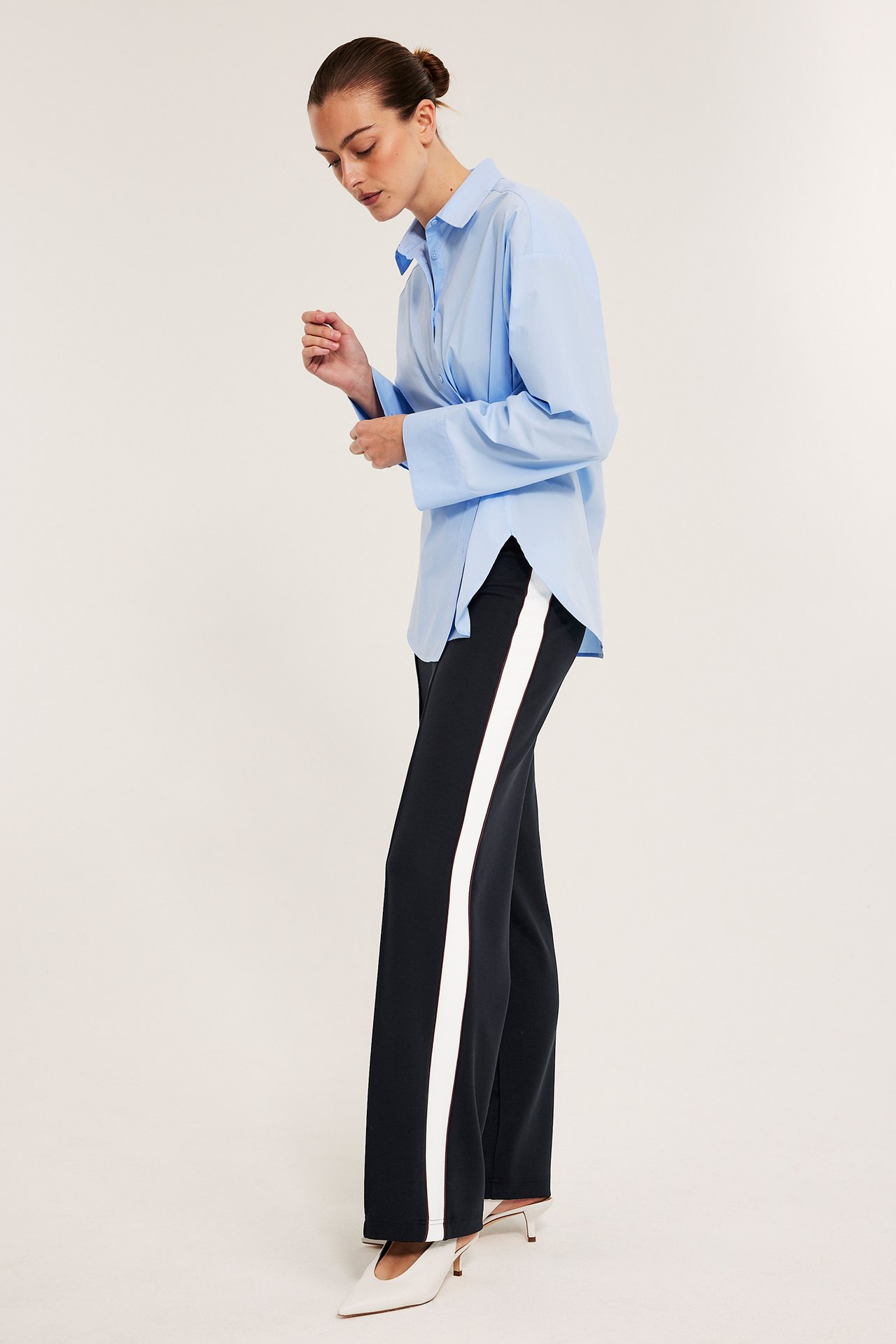 Sivukuva: Nainen tummansinisissä leveissä jerseyhousuissa valkoisella sivuraidalla, vaaleansinisessä paidassa ja valkoisissa muuleissa.