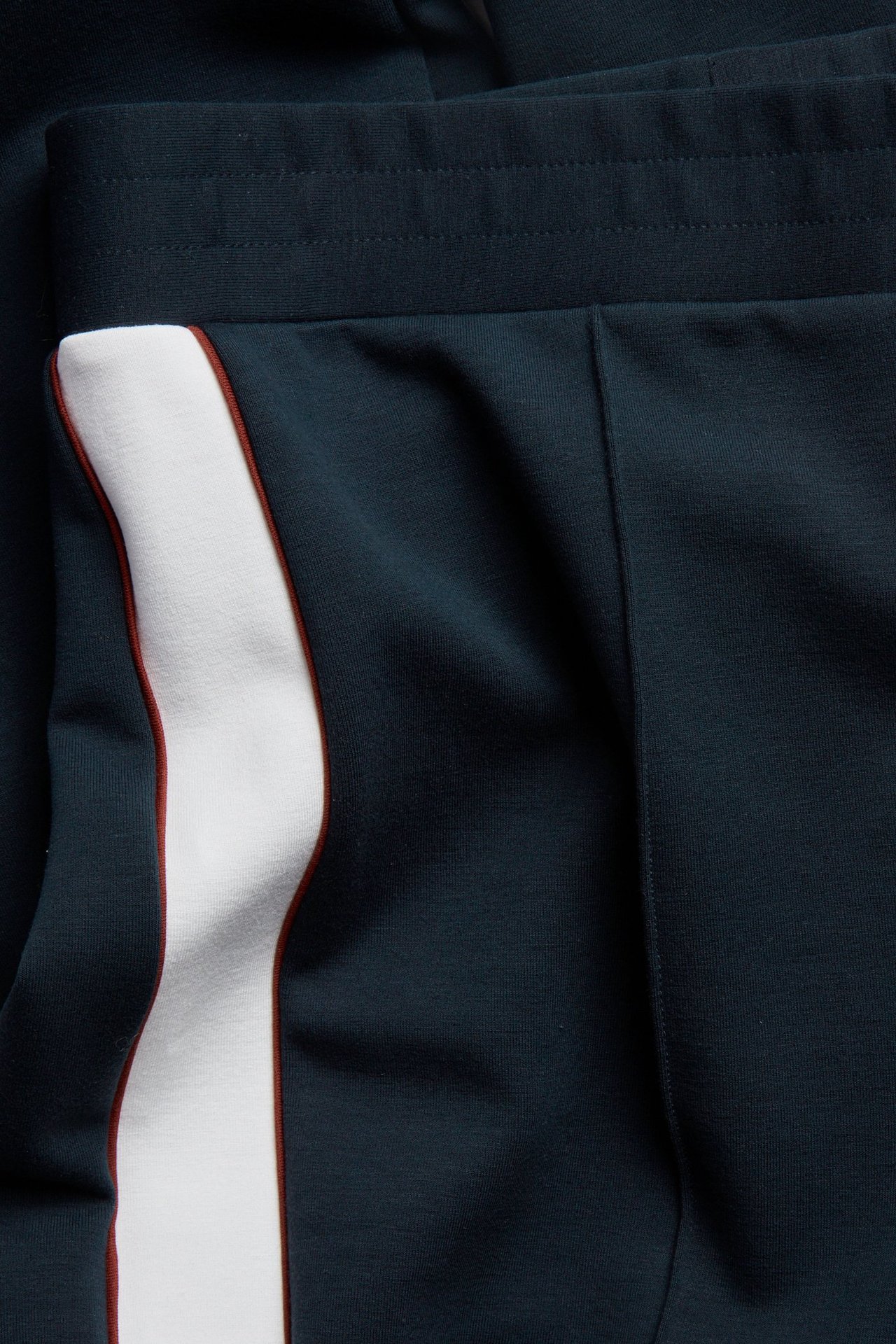 Zbliżenie na ciemnoniebieskie spodnie dresowe z białym paskiem bocznym i przeszytym kantem.