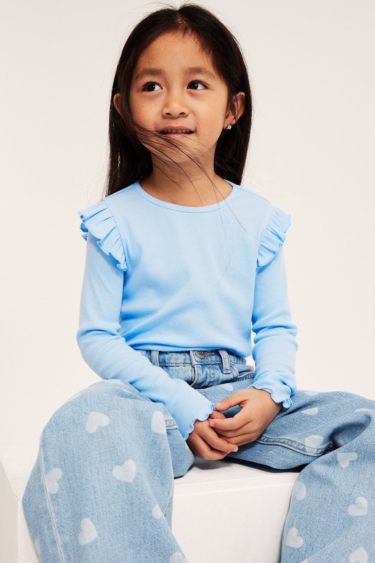 Edestä: Lapsi vaaleansinisessä rypytetyllä ribbipaidassa ja vaaleansinisissä sydänkuvioiduissa farkuissa.