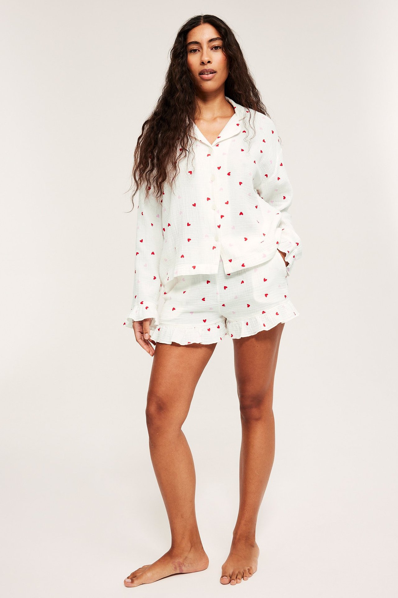 Edestä: Nainen valkoisessa pyjamapaidassa punaisella sydänkuviolla, röyhelöhihansuilla ja yhteensopivilla shortseilla.