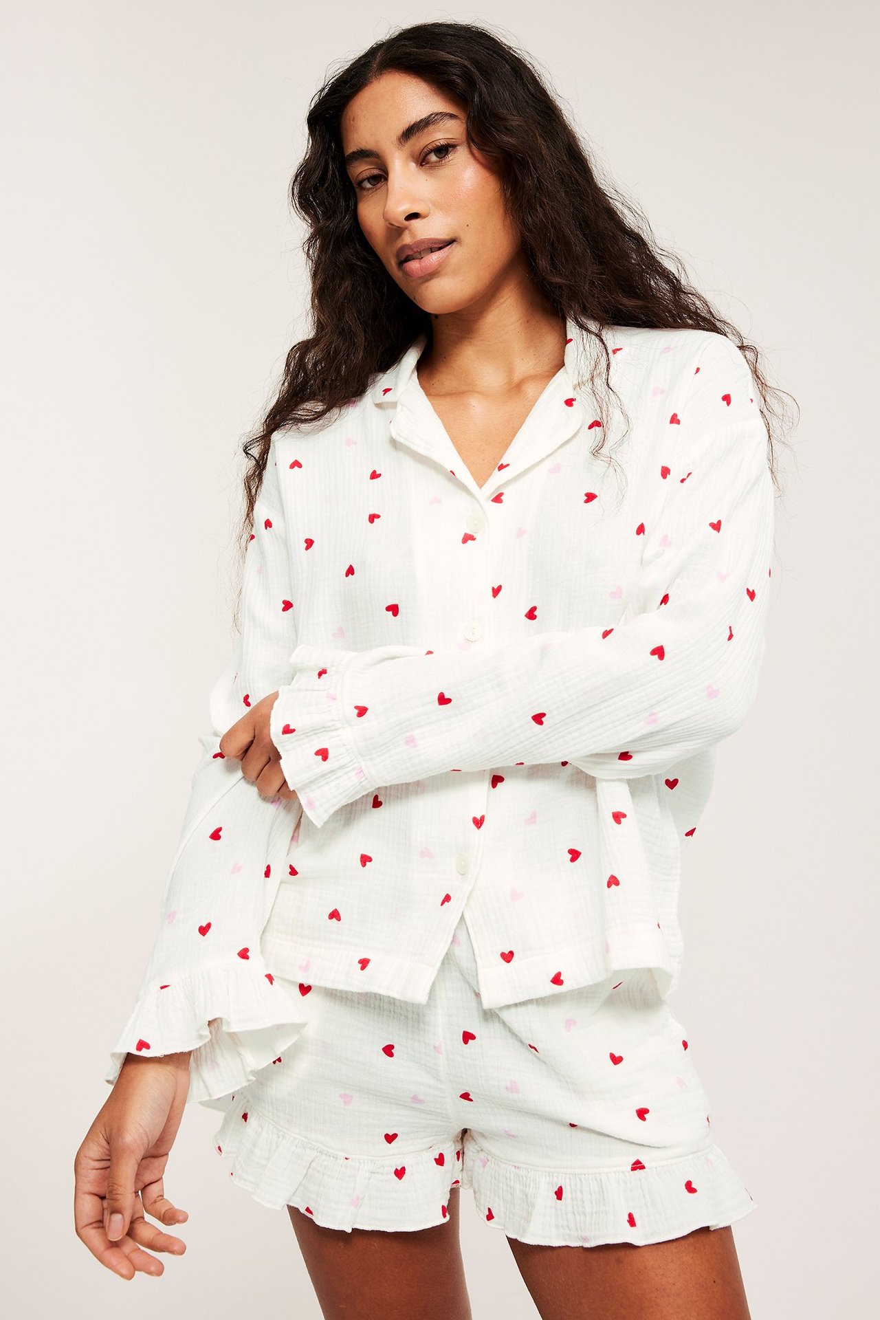 Edestäpäin: Nainen valkoisessa puuvillapyjamapaidassa, jossa punaisia sydämiä, röyhelöhihansuut ja yhteensopivat shortsit.