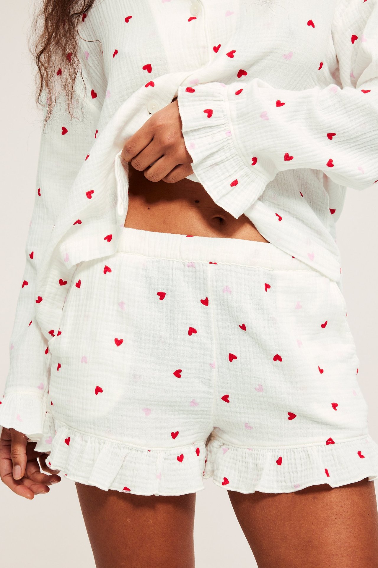 Edestä: Nainen luonnonvalkoisissa pyjamashortseissa punaisilla sydämillä, röyhelöillä ja yhteensopivalla paidalla.
